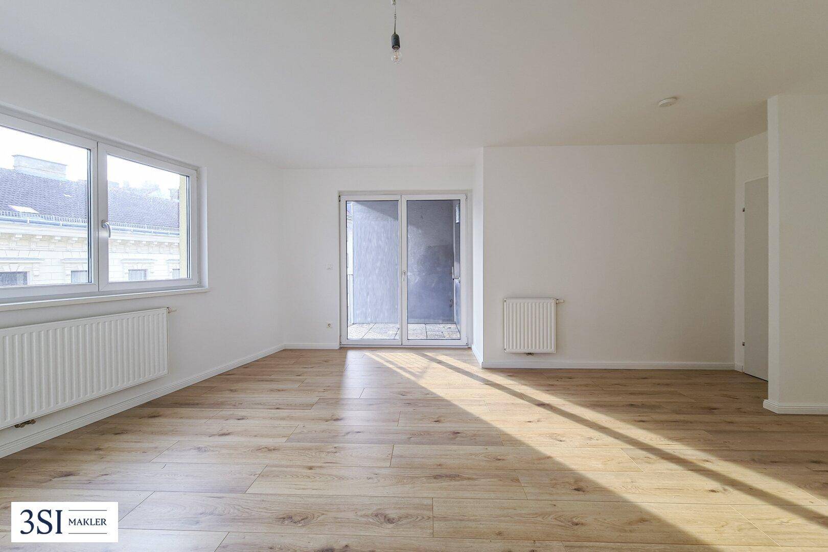 Geräumiges, helles Wohnzimmer mit Holzboden und Zugang zu einem Balkon, ideal für individuelle Gestaltung.