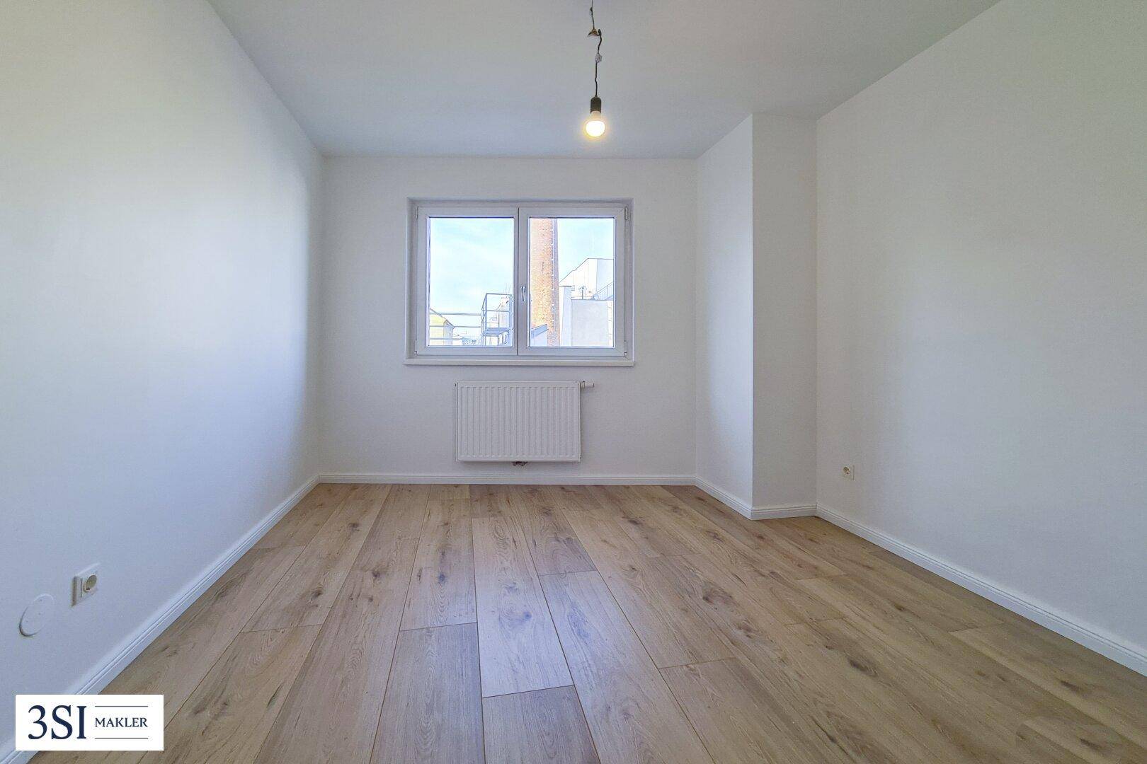 Geräumiges Schlafzimmer mit Holzboden und einem großen Fenster, das für eine angenehme Helligkeit sorgt.