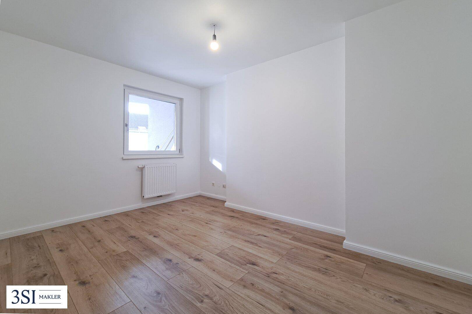 Helles Schlafzimmer mit Holzboden und einem Fenster, das viel Tageslicht in den Raum lässt.