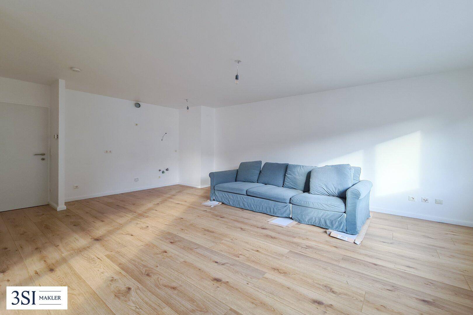 Heller Wohnbereich mit Holzboden und einem blauen Sofa, bereit für persönliche Einrichtung und Gestaltung.