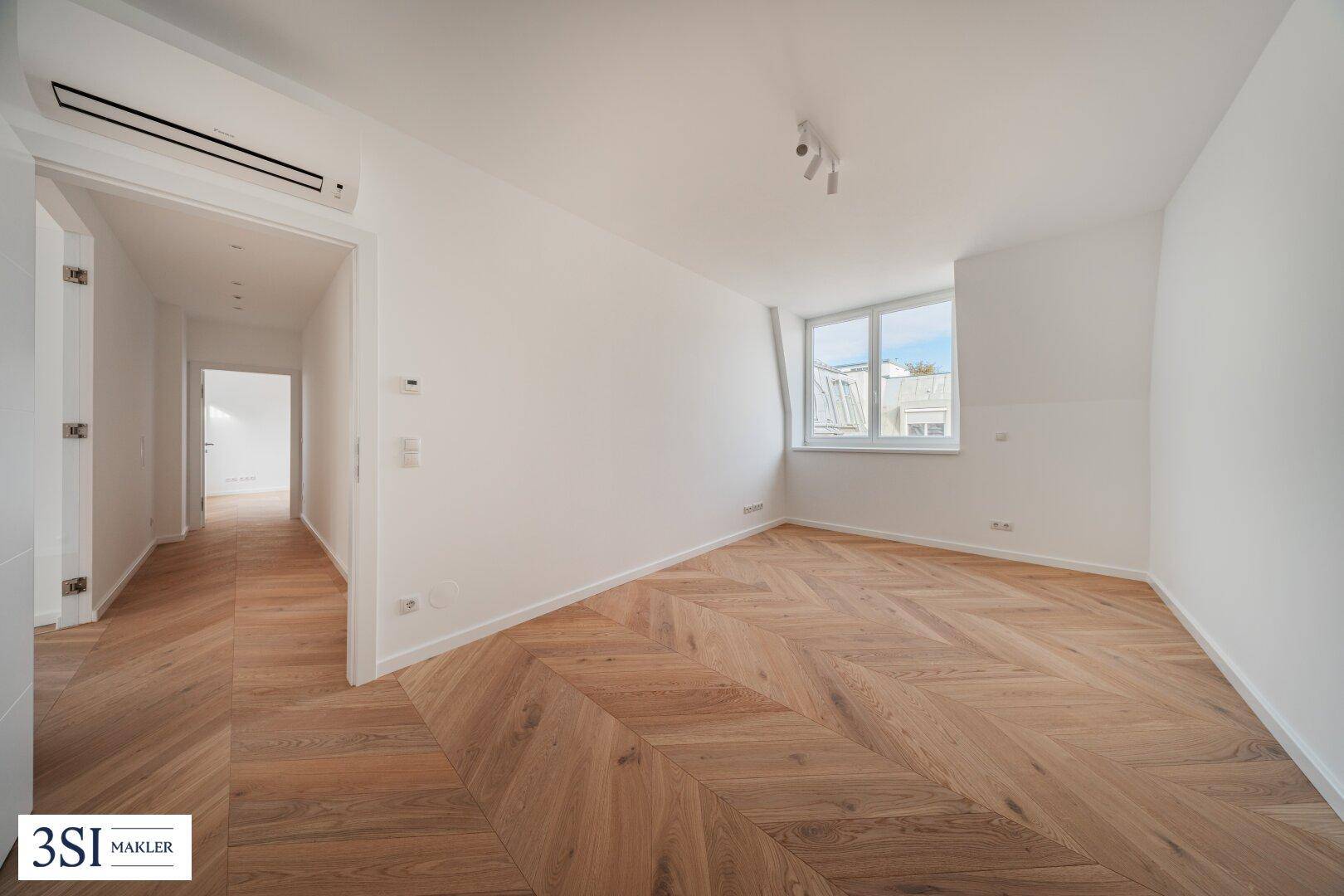 Helles Schlafzimmer mit Fischgrätparkett, Fenster und Zugang zu einem Flur.
