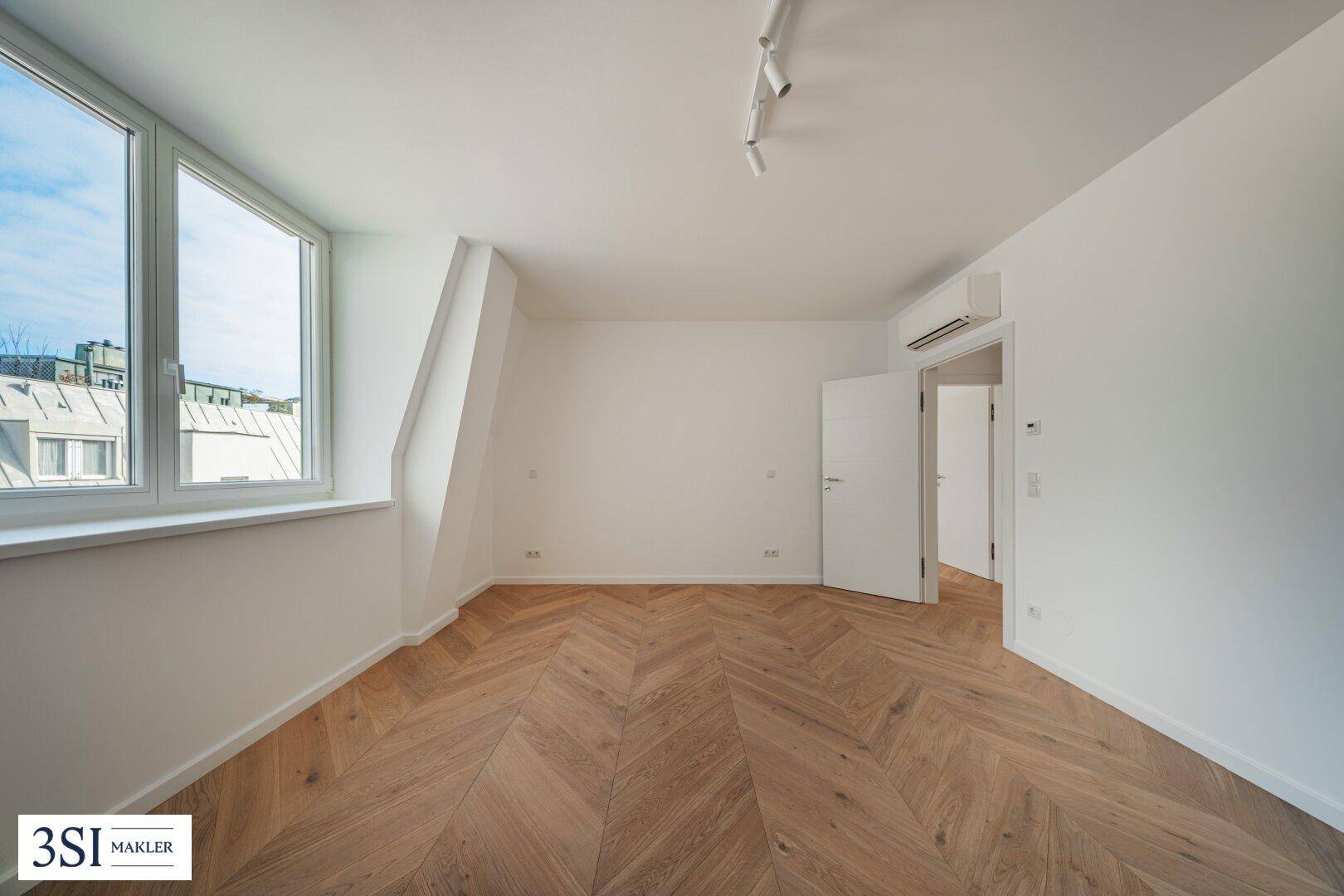 Geräumiges Schlafzimmer mit Fischgrätparkett, Klimaanlage und Dachschräge, die Charakter verleiht.