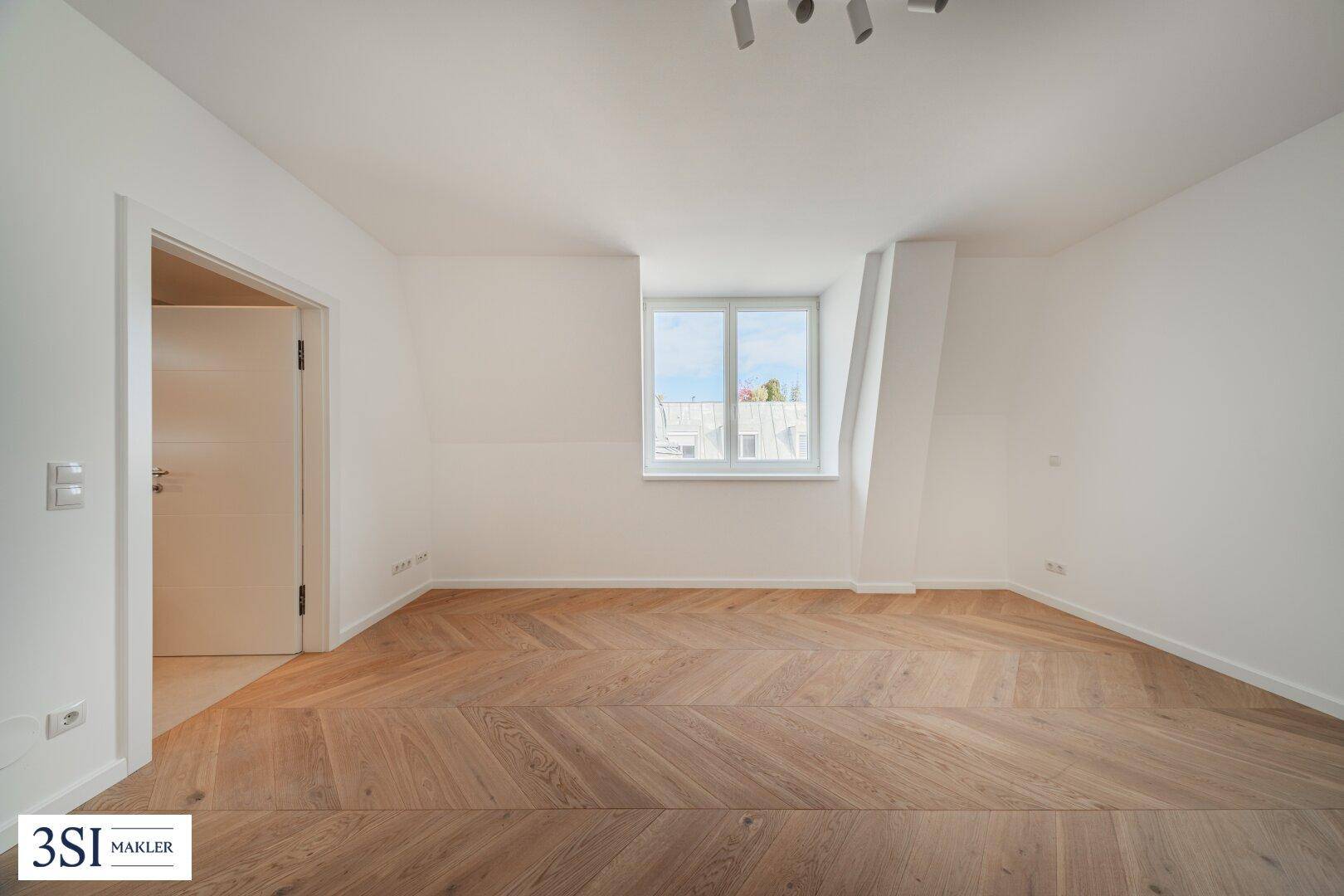 Helles Schlafzimmer mit Fischgrätparkett, Dachschräge und Fenster mit Blick nach draußen.