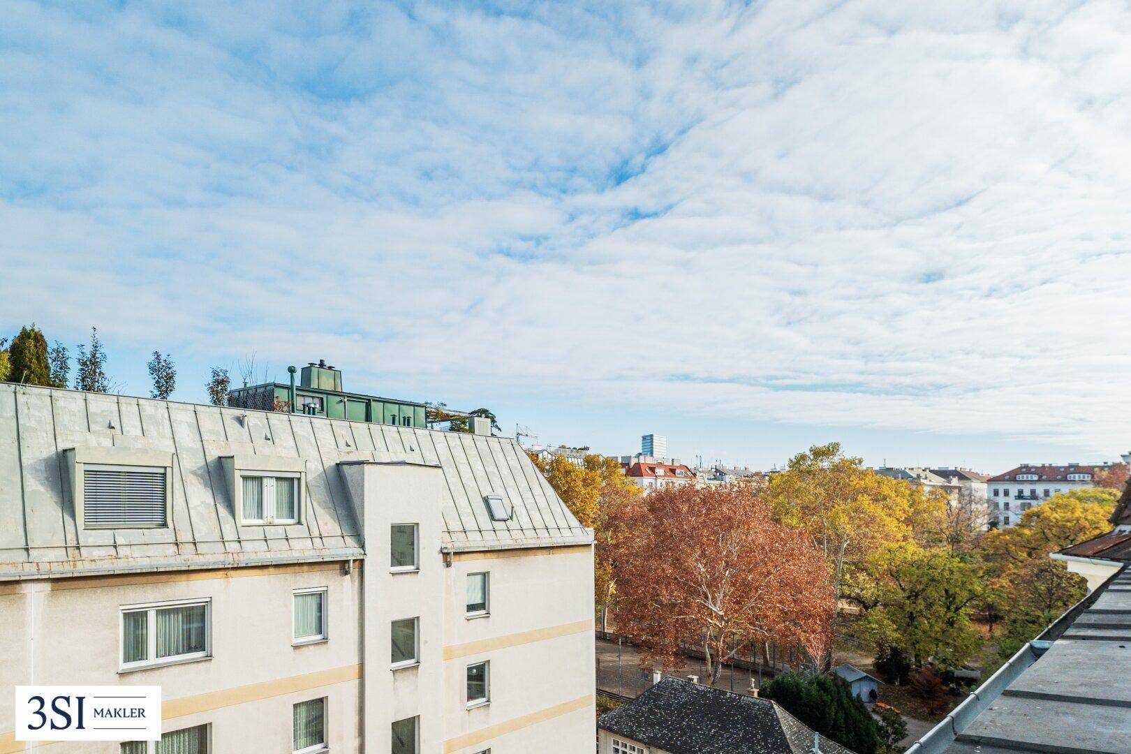 Blick über die Dächer der Stadt mit herbstlicher Baumkulisse und umliegenden Gebäuden.