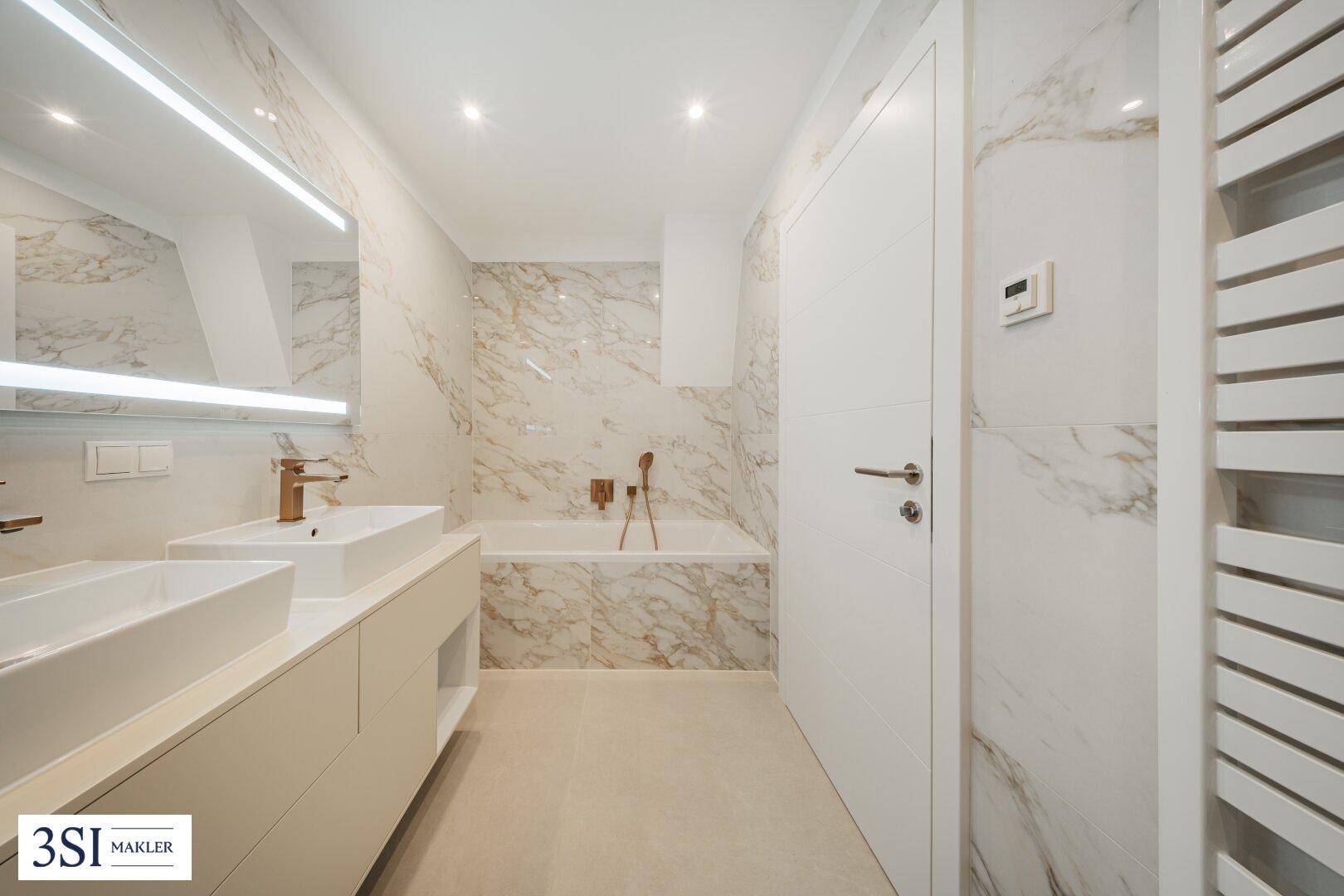 Luxuriöses Badezimmer mit Marmorfliesen, Doppelwaschbecken, Badewanne und beheiztem Handtuchhalter.