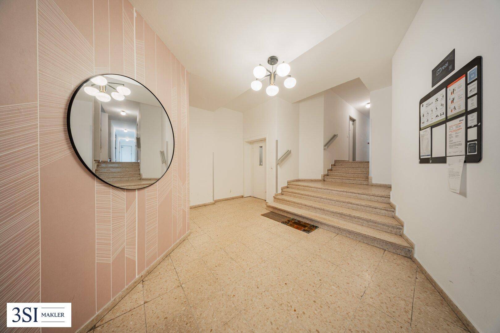 Heller Eingangsbereich mit Terrazzoboden, Treppe und einem großen runden Spiegel an der Wand.