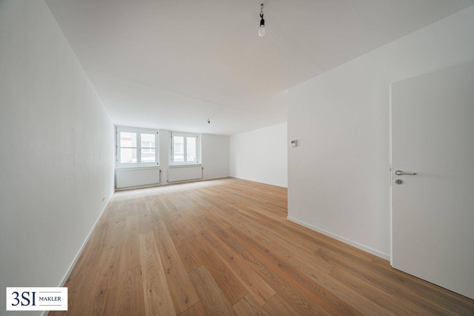 Helles, leeres Zimmer mit Holzboden und zwei Fenstern, bereit für individuelle Gestaltung.