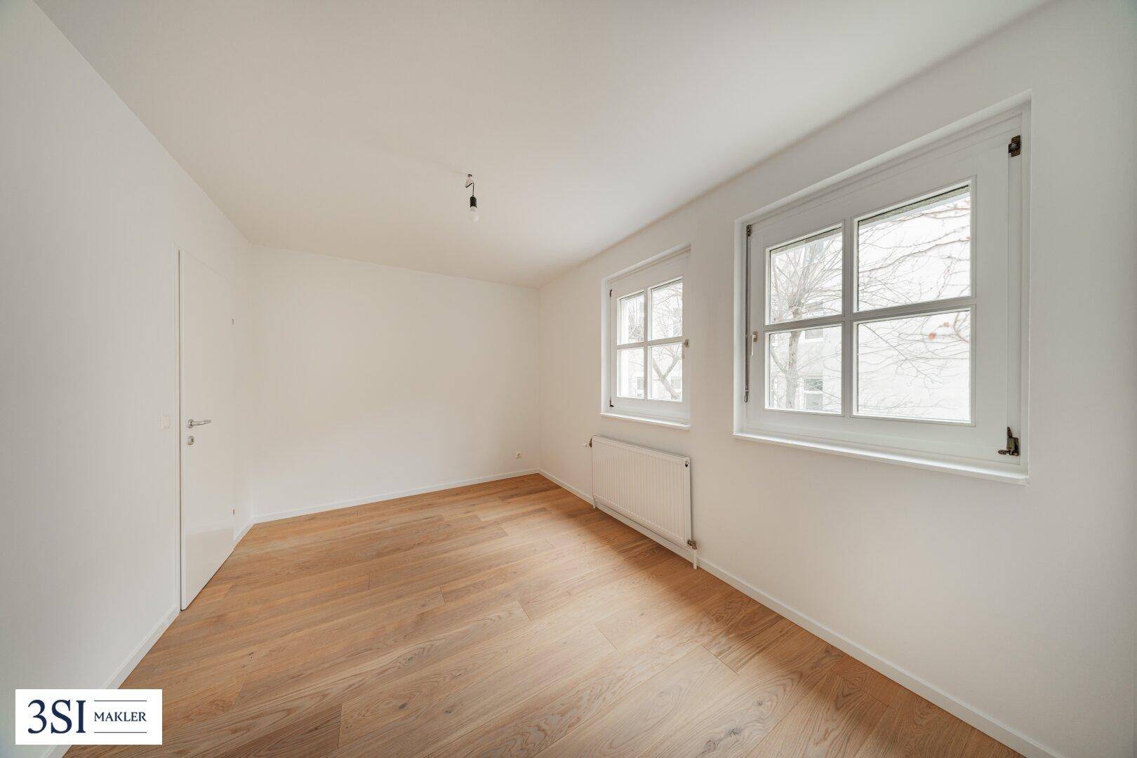 Ruhiges, helles Schlafzimmer mit Holzboden und zwei Fenstern, ideal für erholsame Nächte.
