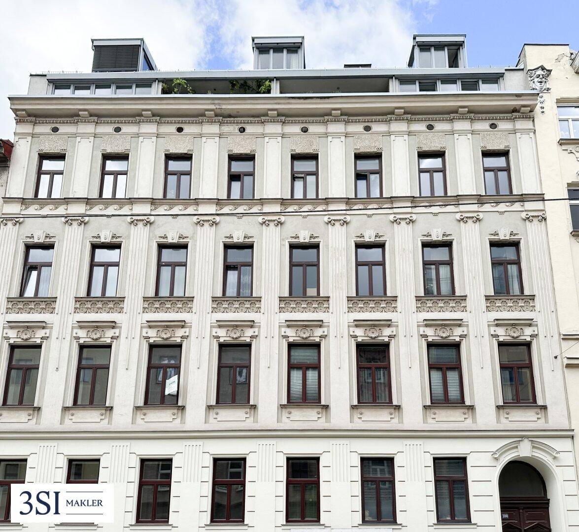 Historische Fassade eines Mehrfamilienhauses mit modernem Dachausbau und vielen Fenstern.