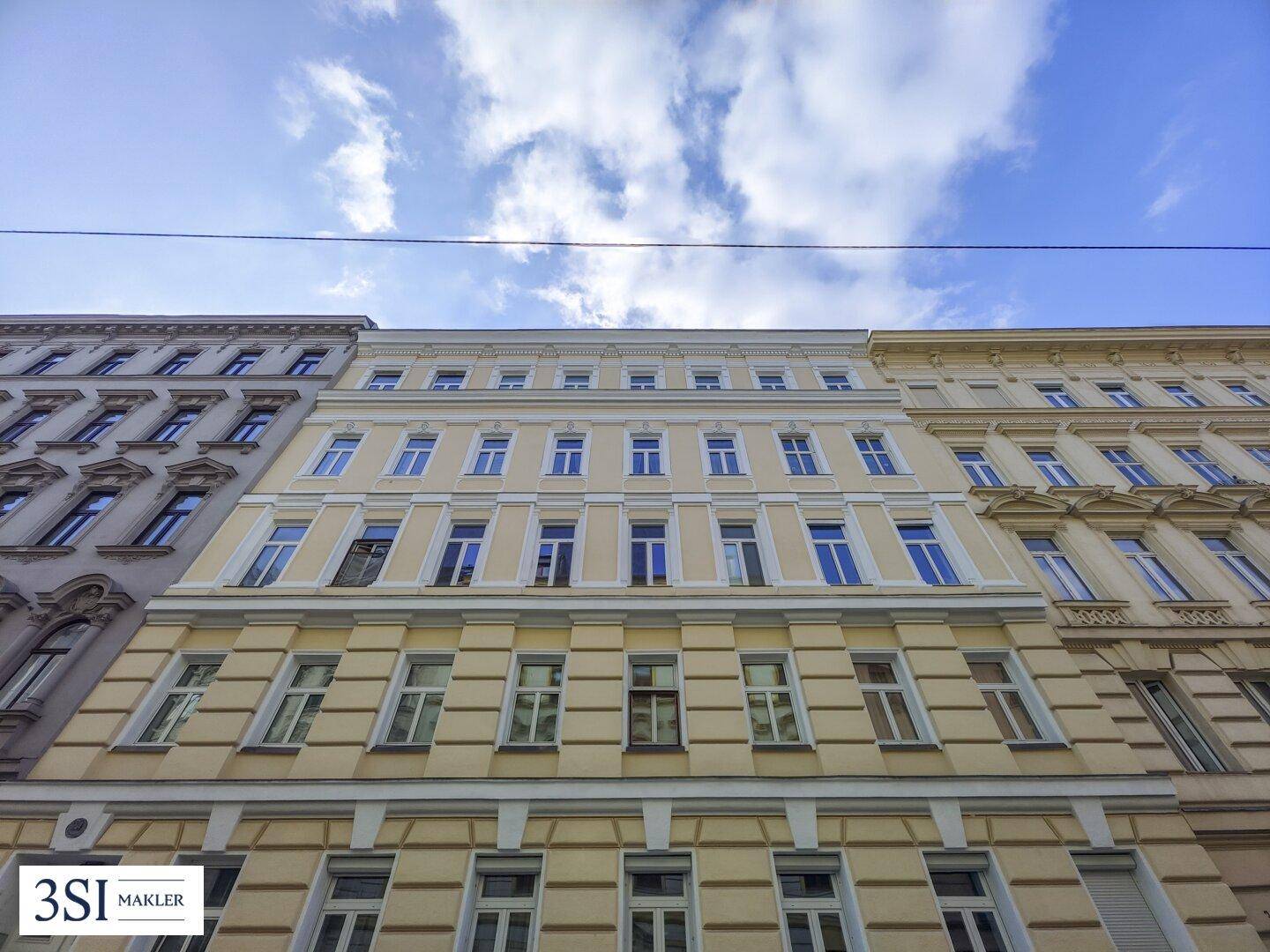 Die imposante Fassade eines Altbaus mit vielen Fenstern und klassischer Architektur unter blauem Himmel.