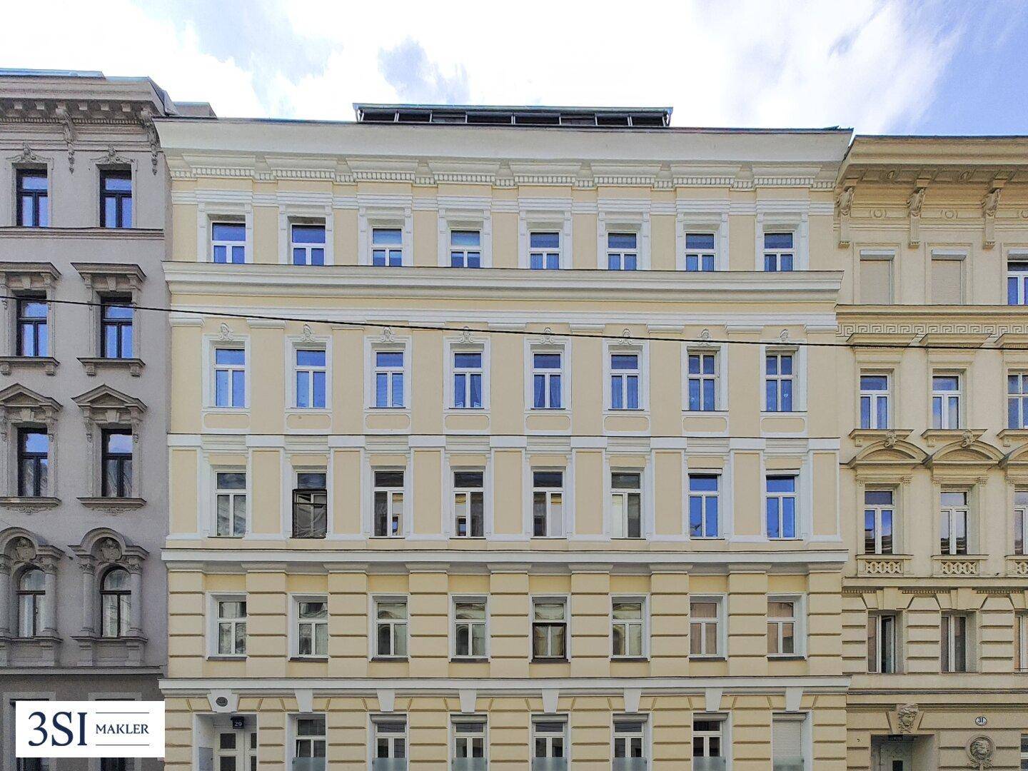 Die breite, klassische Fassade eines Altbaus mit zahlreichen Fenstern und eleganter Gestaltung.