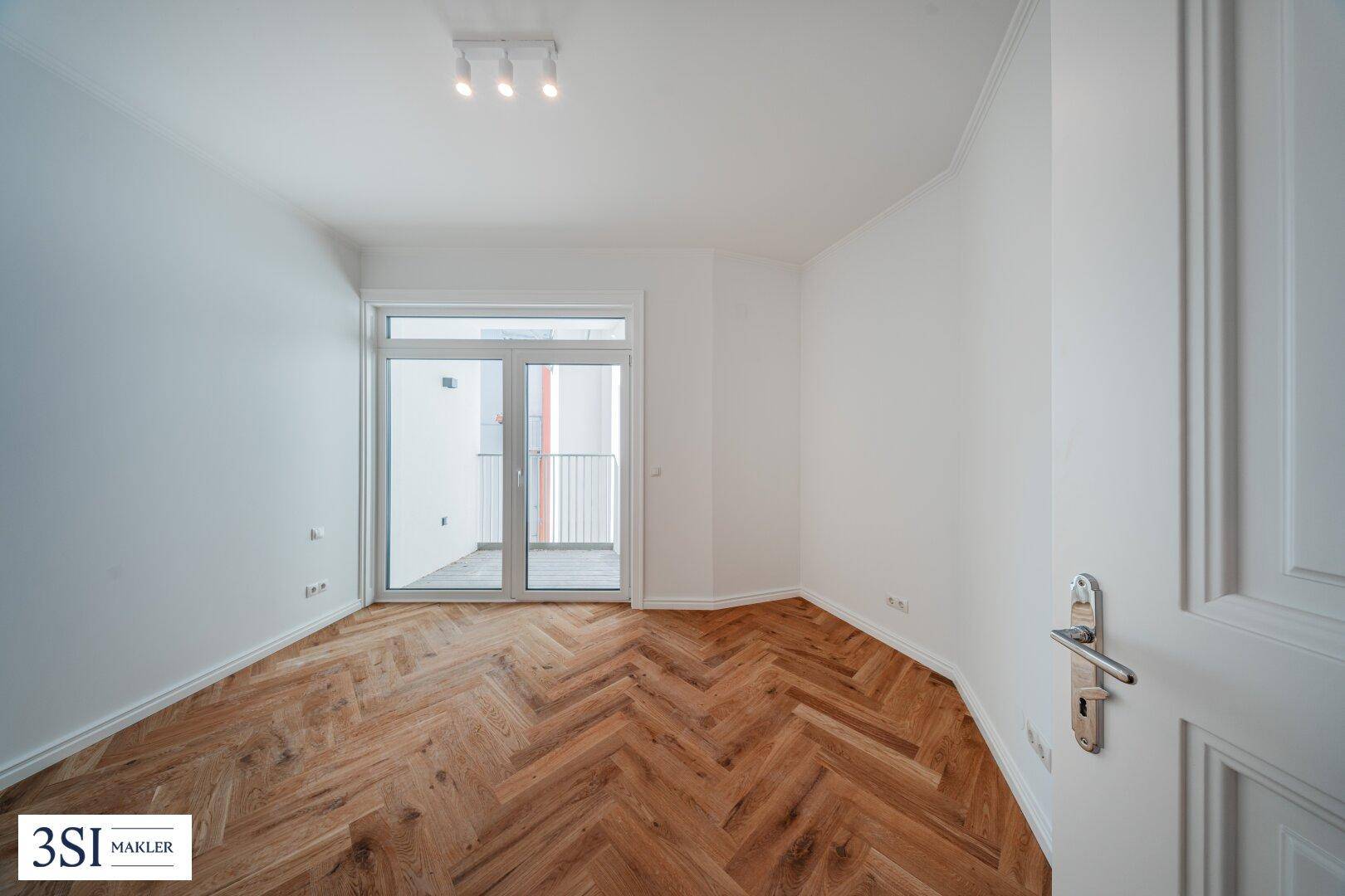 Heller Raum mit Fischgrätparkett und Zugang zu einem französischen Balkon, frisch renoviert.