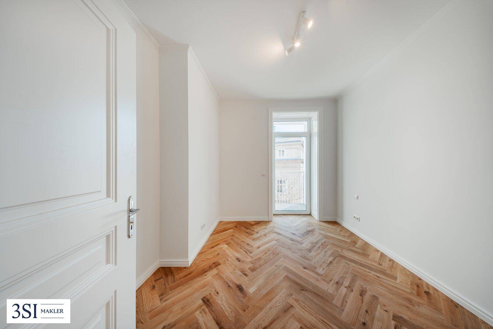 Helles Zimmer mit Fischgrätparkett und Zugang zu einem kleinen Balkon, ideal für ein Schlafzimmer.