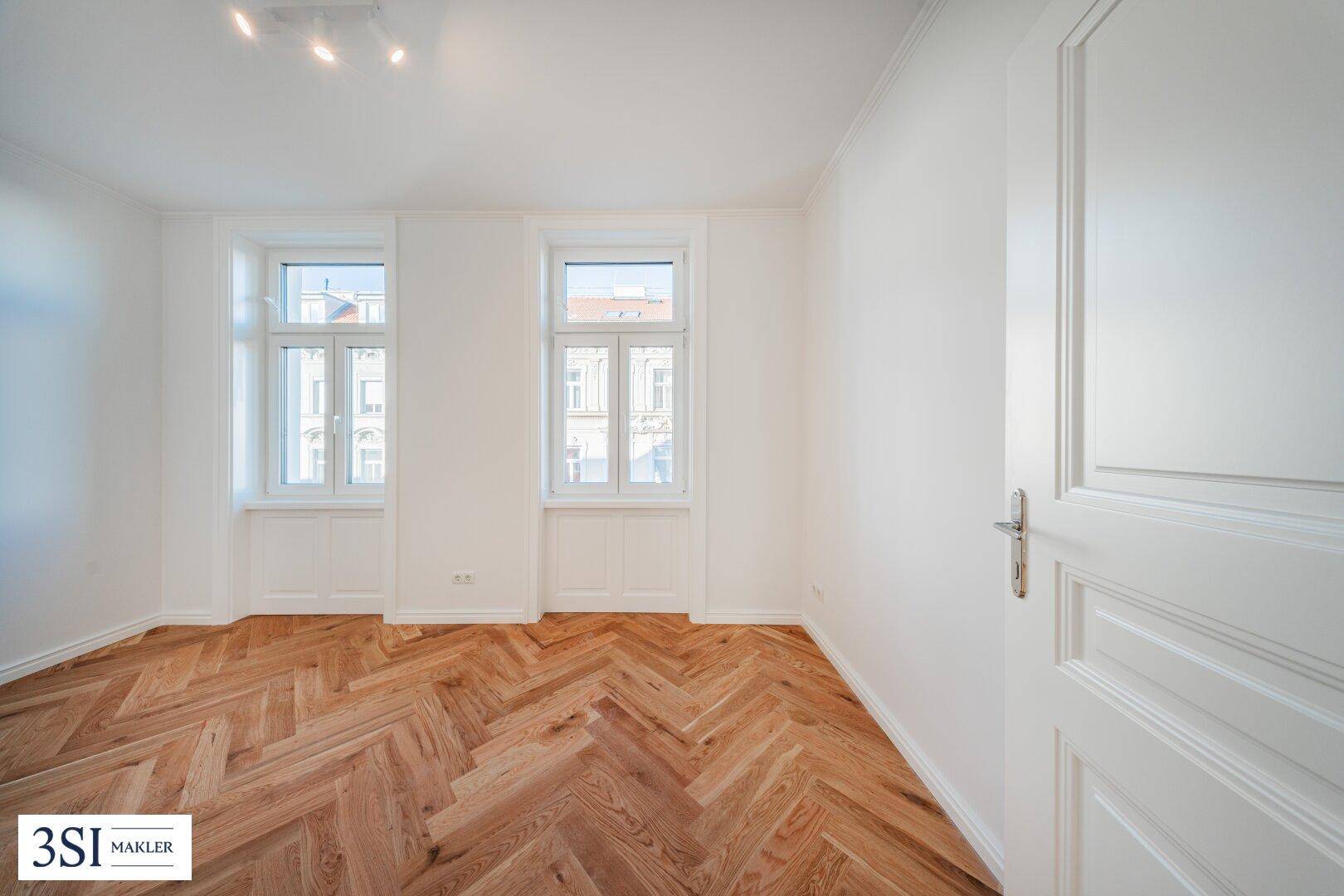 Heller Raum mit elegantem Fischgrätparkett und hohen Fenstern, ideal als Wohn- oder Schlafzimmer.
