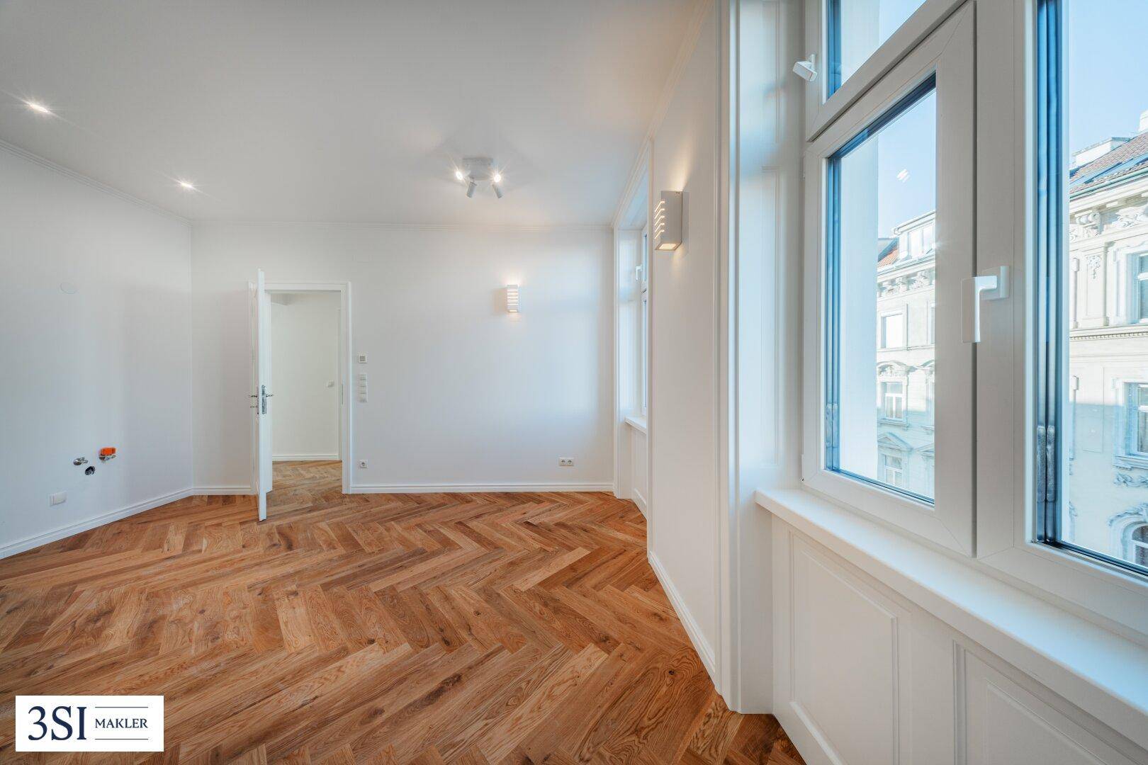 Lichtdurchfluteter Raum mit klassischem Fischgrätparkett und Blick auf die umliegenden Gebäude.