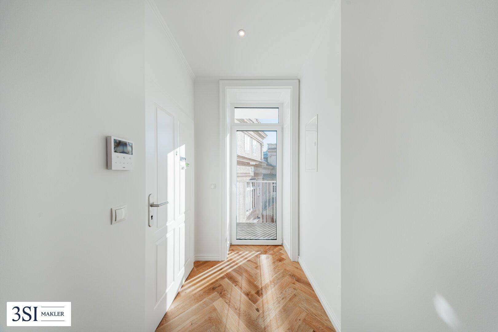 Heller Flur mit Fischgrätparkett und Gegensprechanlage, führt zu einem französischen Balkon.