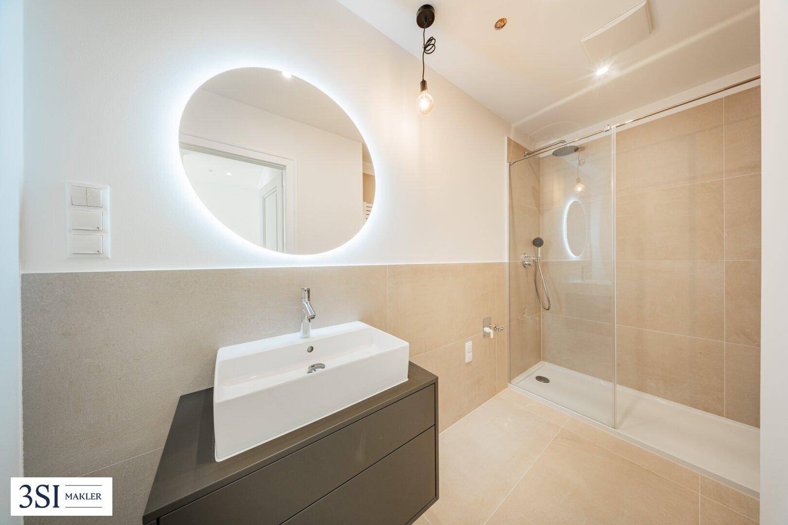 Modernes Badezimmer mit großem beleuchtetem Spiegel, Einzelwaschbecken und ebenerdiger Dusche.