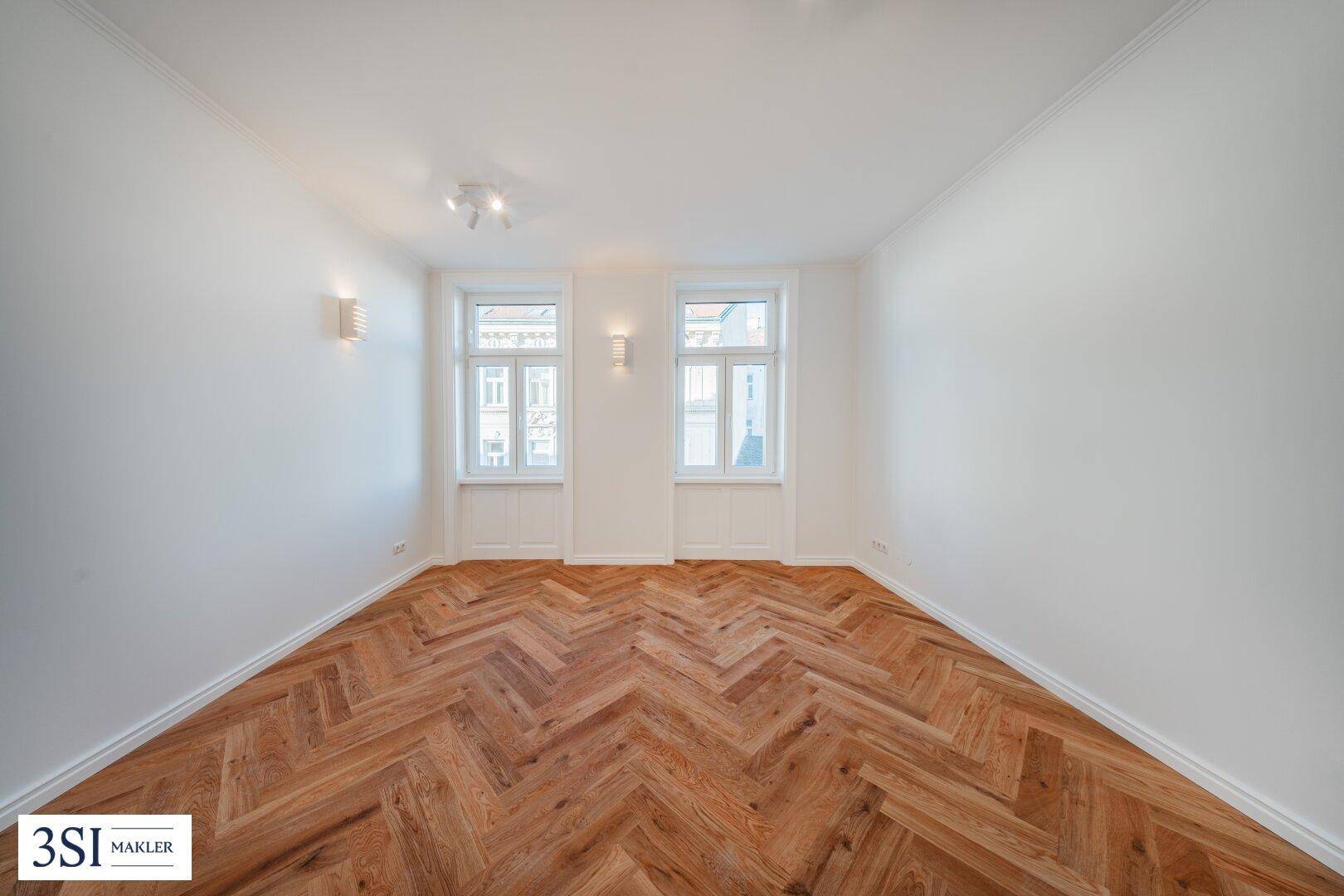 Helles Zimmer mit Fischgrätparkett und zwei großen Fenstern, ideal für Wohn- oder Schlafbereich.
