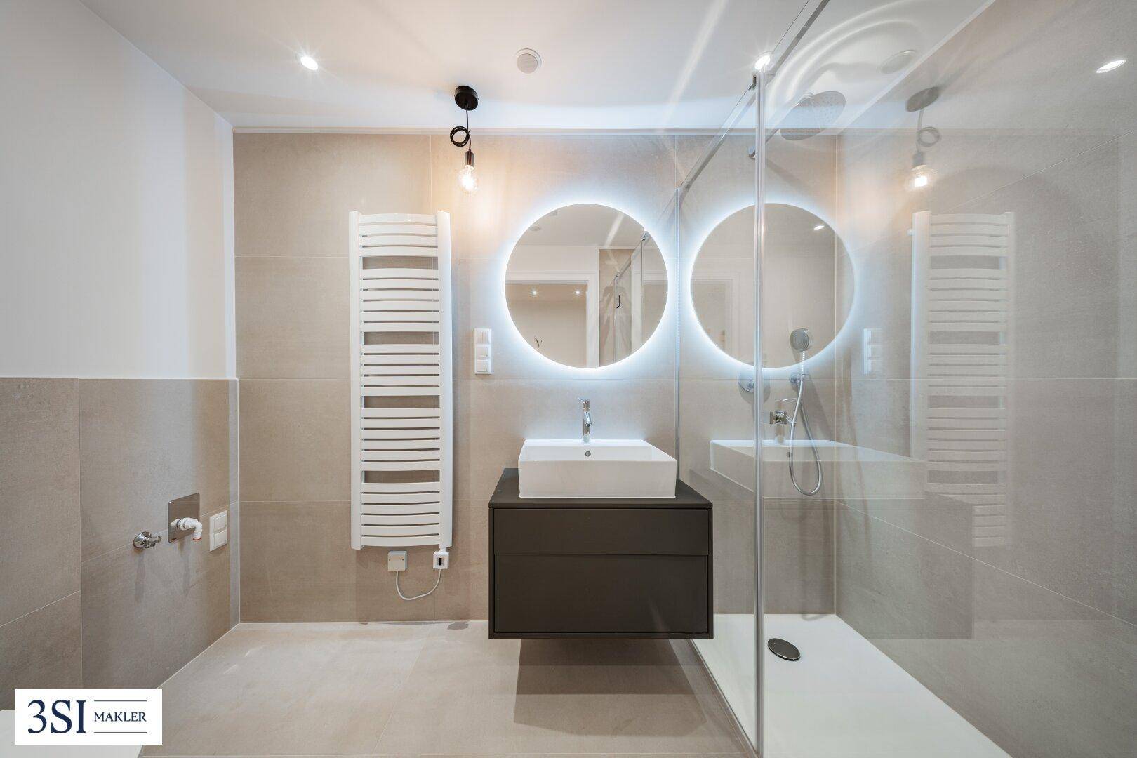 Modernes Badezimmer mit begehbarer Dusche, Doppelwaschbecken und beleuchteten Spiegeln.