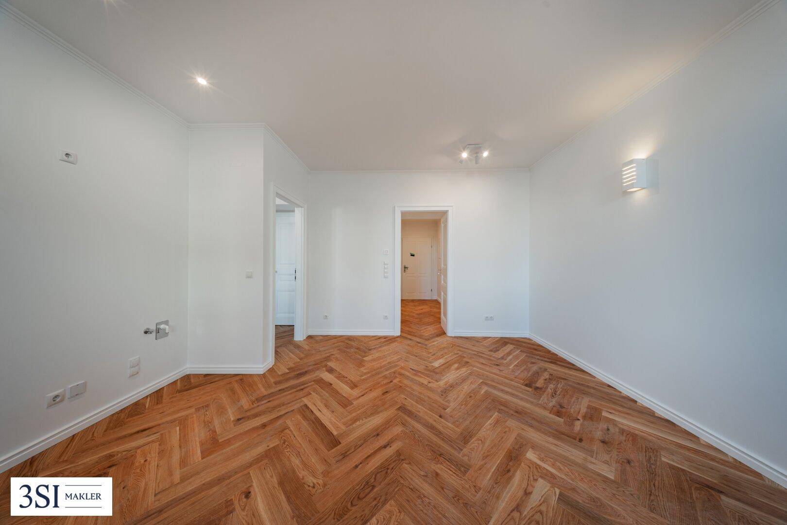 Renoviertes Wohnzimmer mit elegantem Fischgrätparkett und mehreren Türöffnungen, die zu anderen Räumen führen.