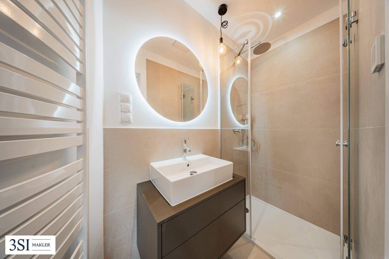 Modernes Badezimmer mit begehbarer Dusche, stilvollem Waschtisch und beleuchtetem Spiegel.