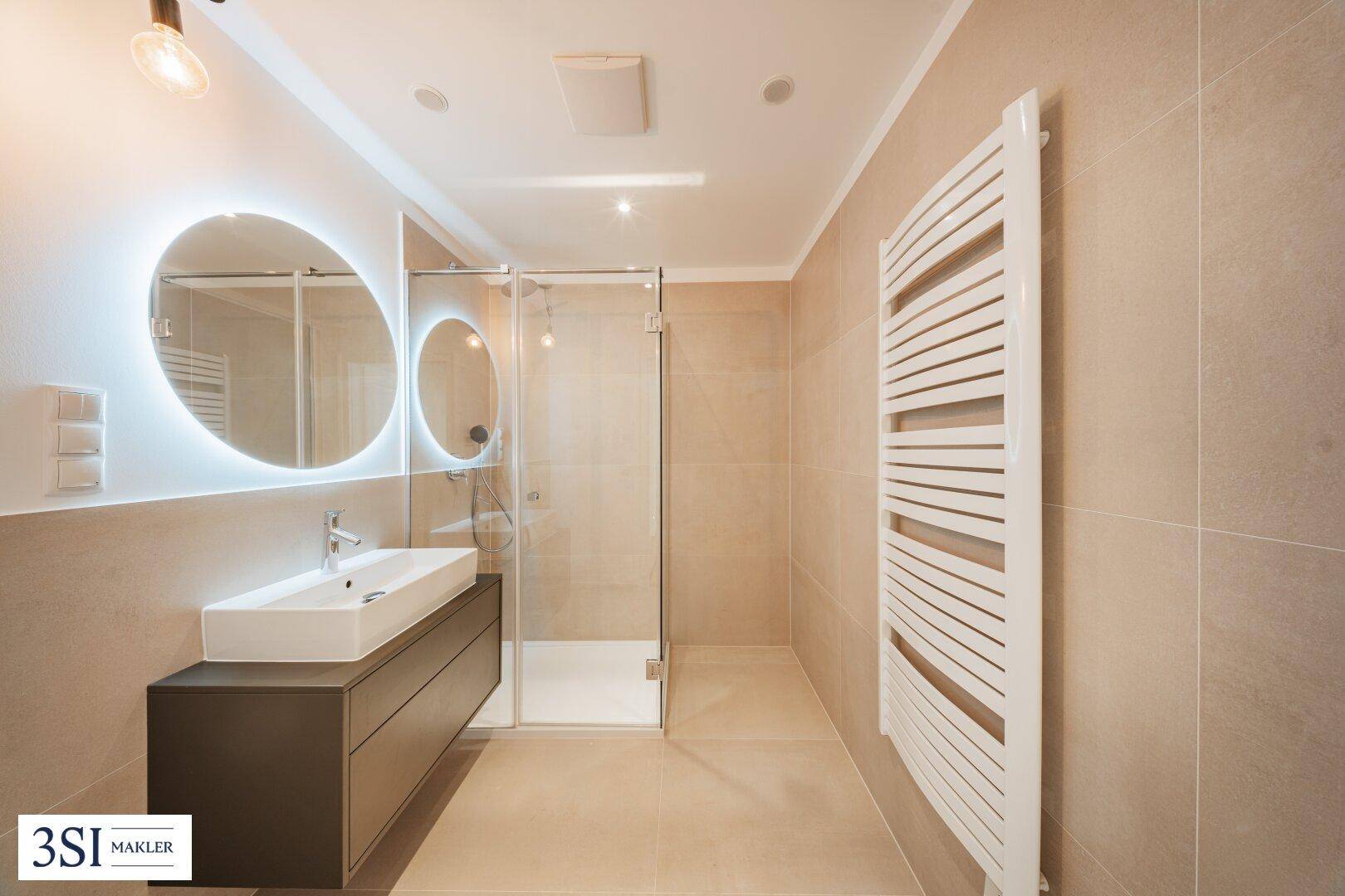 Modernes Badezimmer mit begehbarer Dusche, beleuchtetem Spiegel und Handtuchheizkörper.