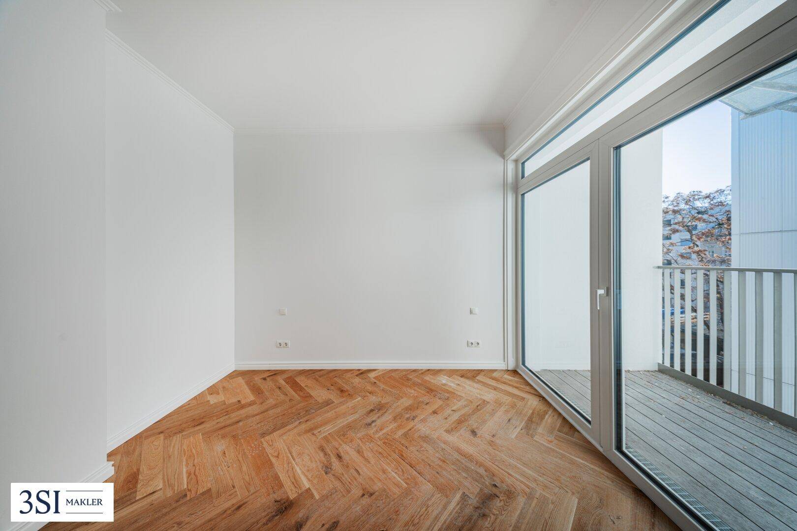 Heller Raum mit Fischgrätparkett und großem Zugang zu einem Balkon.