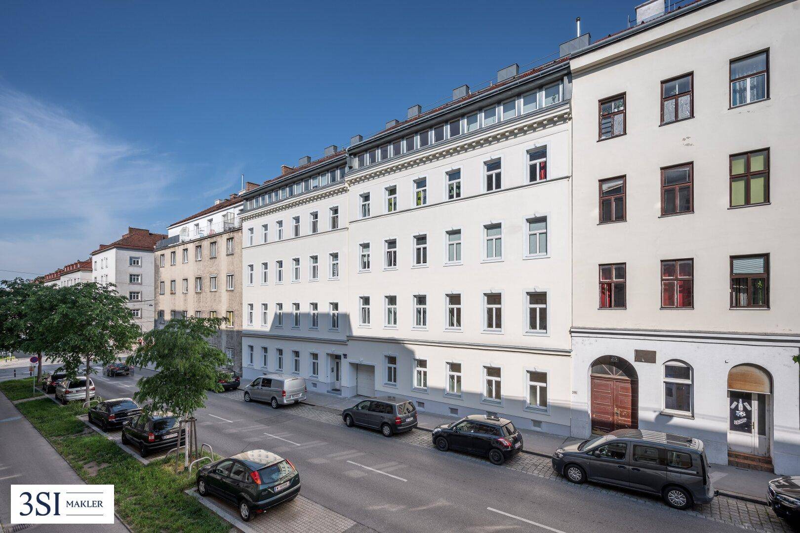 Die gepflegte Fassade eines klassischen Wiener Altbaus mit vielen Fenstern und Parkplätzen an der Straße.