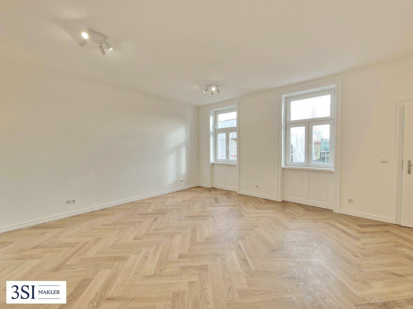 Helles, leeres Zimmer mit Fischgrätparkett und zwei Fenstern, bereit zur individuellen Gestaltung.