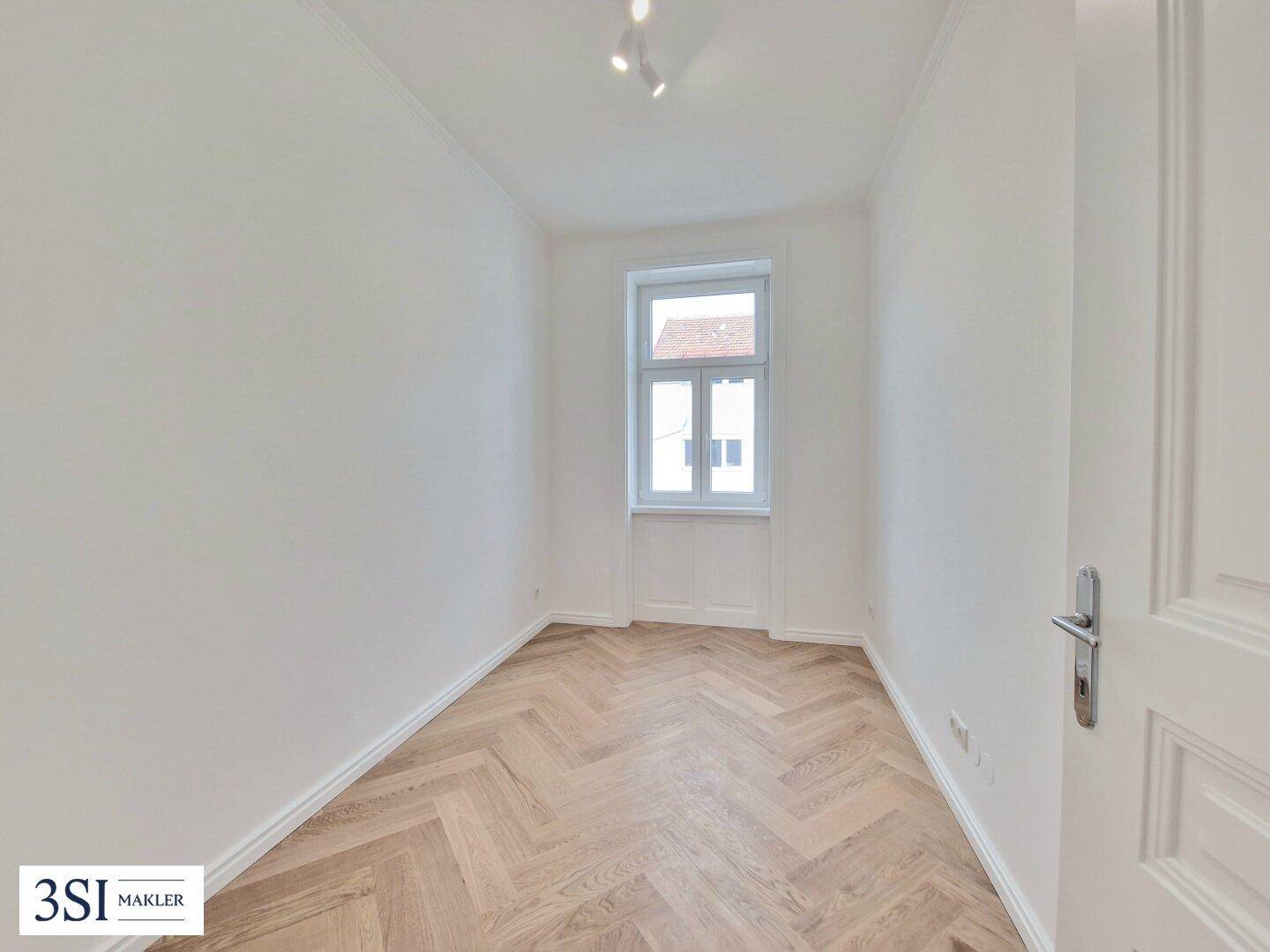 Kleineres, helles Zimmer mit Fischgrätparkett und einem Fenster, perfekt als Kinder- oder Gästezimmer.