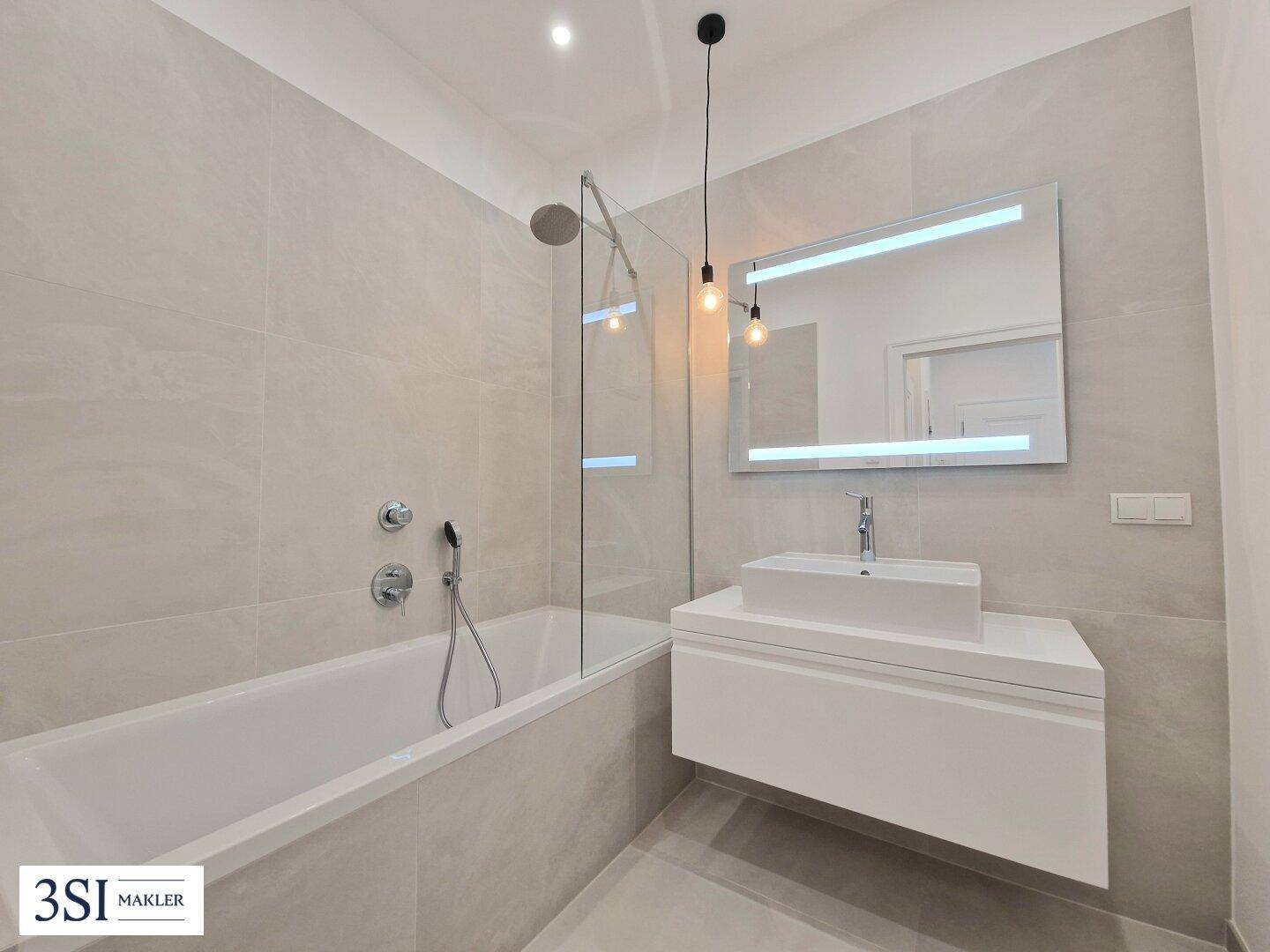 Modernes Badezimmer mit Badewanne, Einzelwaschbecken und beleuchtetem Spiegel.