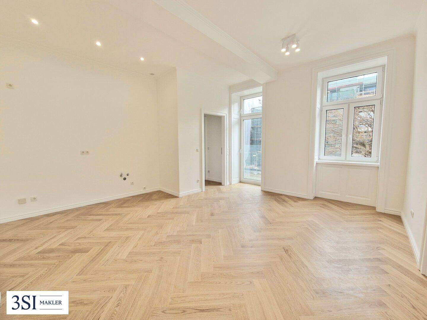 Geräumiges, helles Zimmer mit Fischgrätparkett und Zugang zu einem französischen Balkon.