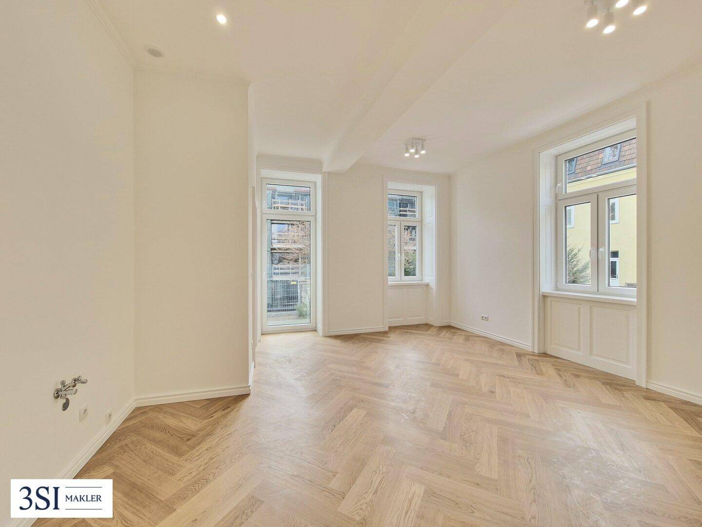 Geräumiges, helles Zimmer mit Fischgrätparkett und Zugang zu einem französischen Balkon.