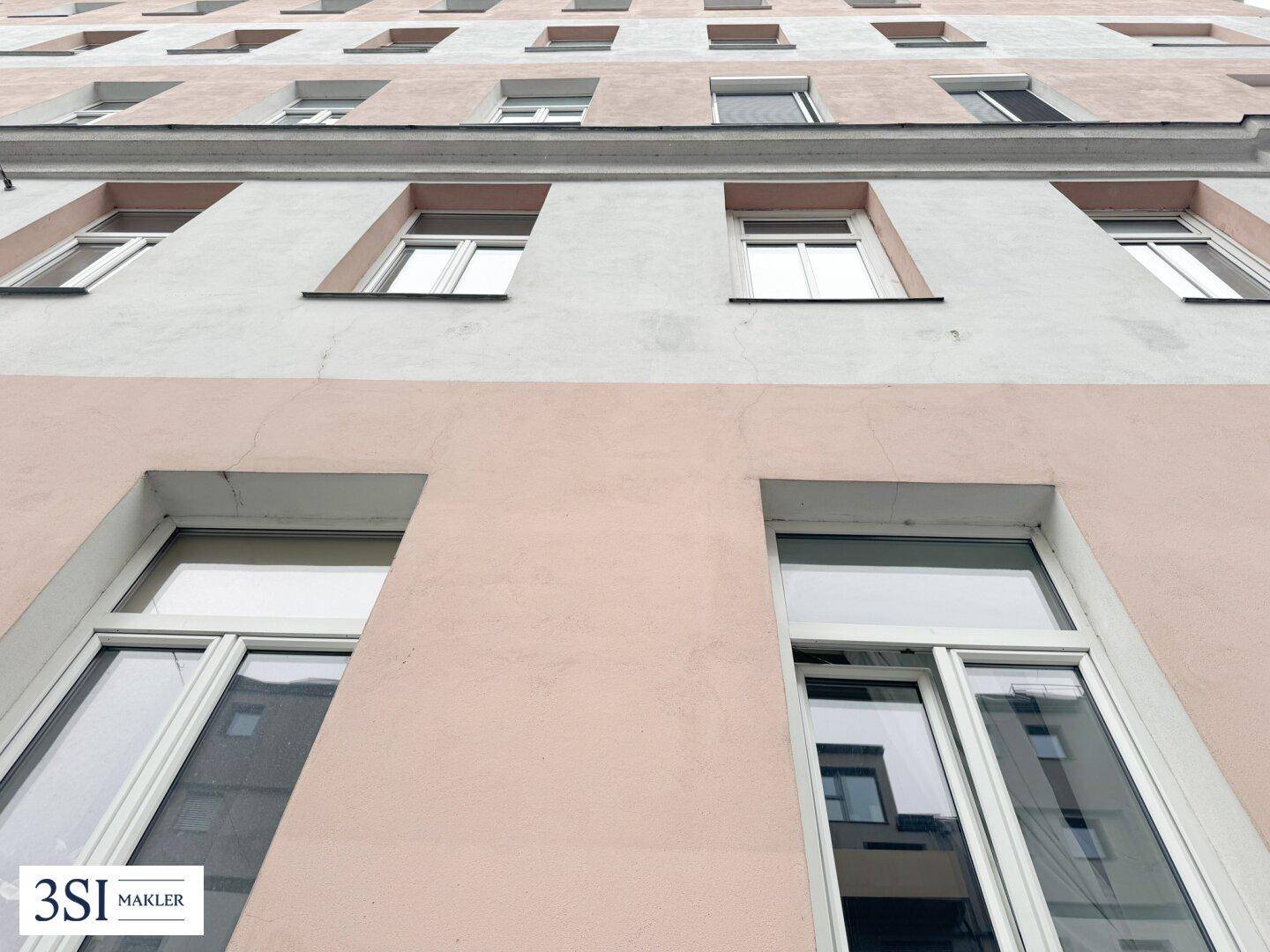 Detailansicht der Fassade eines Altbaus mit regelmäßig angeordneten Fenstern und hellem Anstrich.