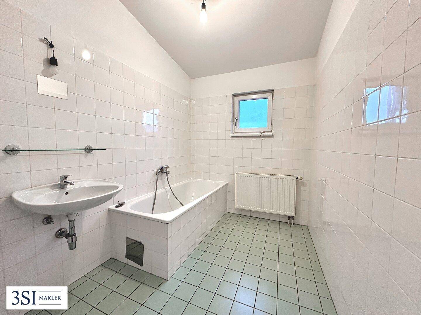Funktionales Badezimmer mit Badewanne, Waschbecken, Fenster und charakteristischen Fliesen aus den 80er Jahren.