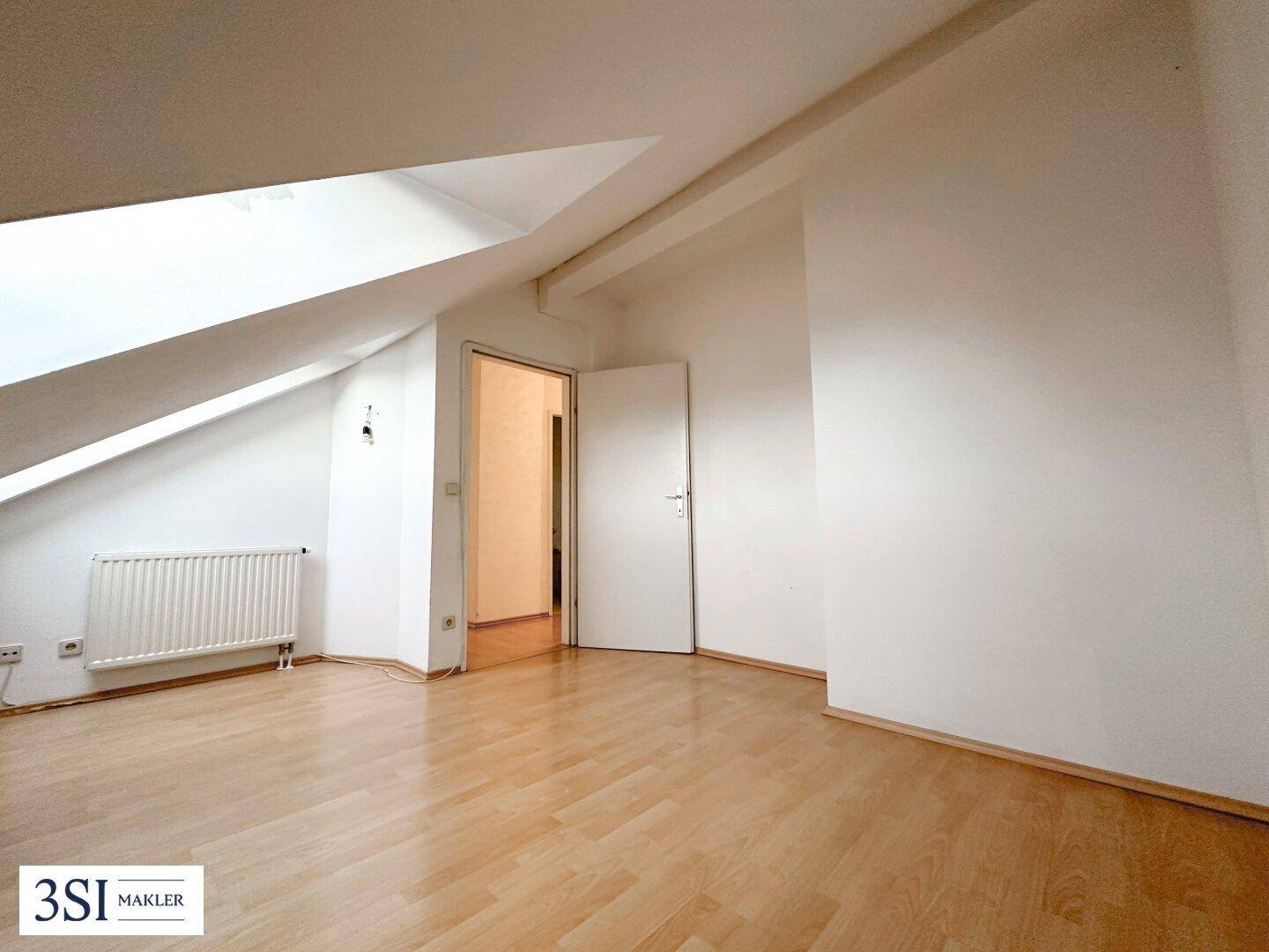 Heller Raum im Dachgeschoss mit schrägen Wänden, Laminatboden und Heizkörper.