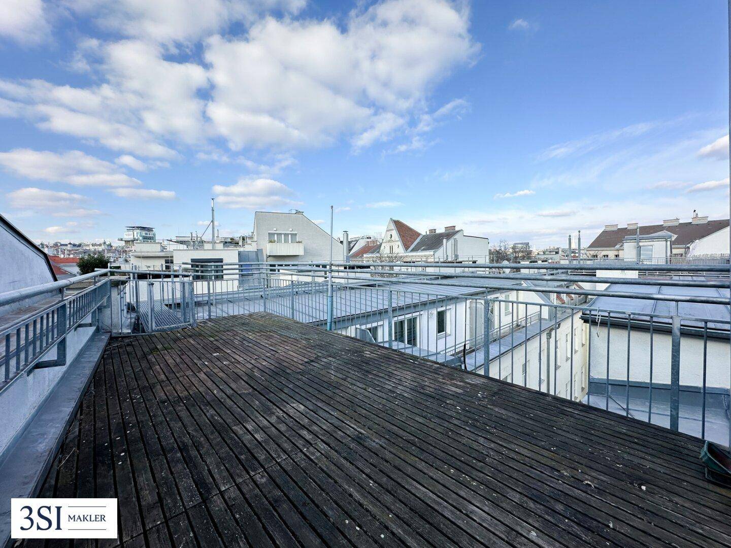 Leere Dachterrasse mit Holzboden und Panoramablick über die umliegenden Dächer der Stadt.