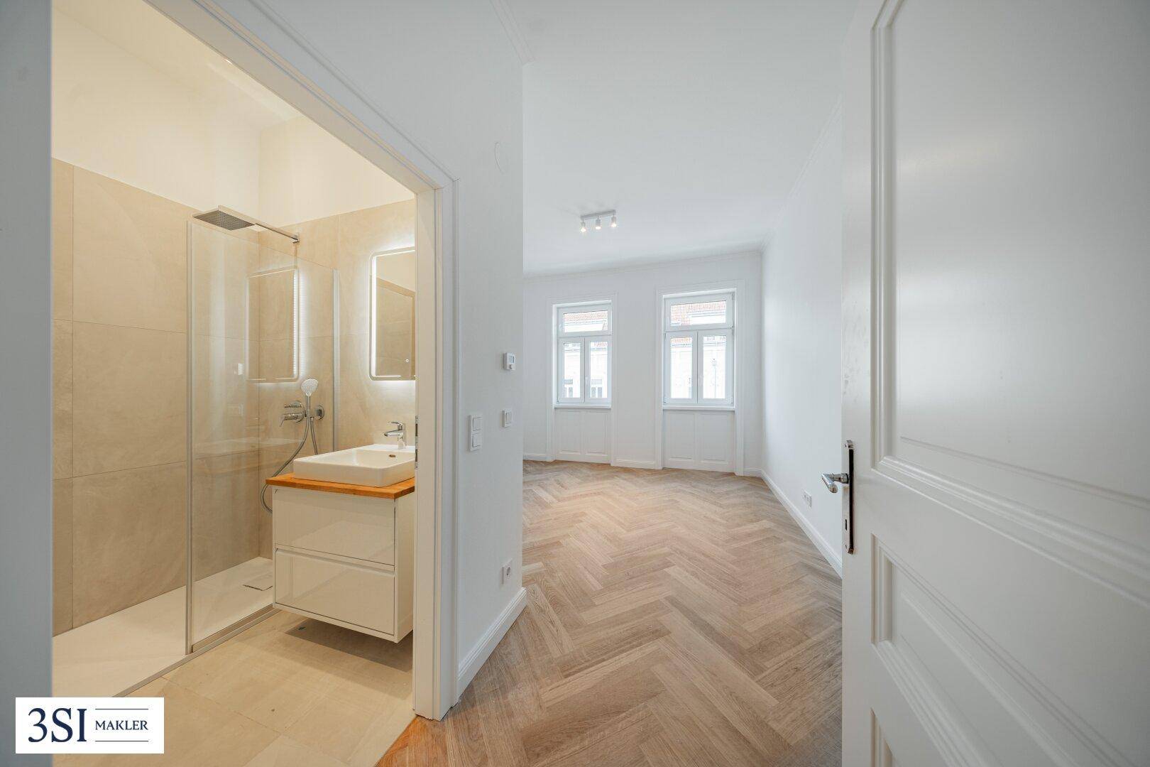 Blick vom Flur in ein modernes Badezimmer mit Dusche und angrenzendem hellen Zimmer.