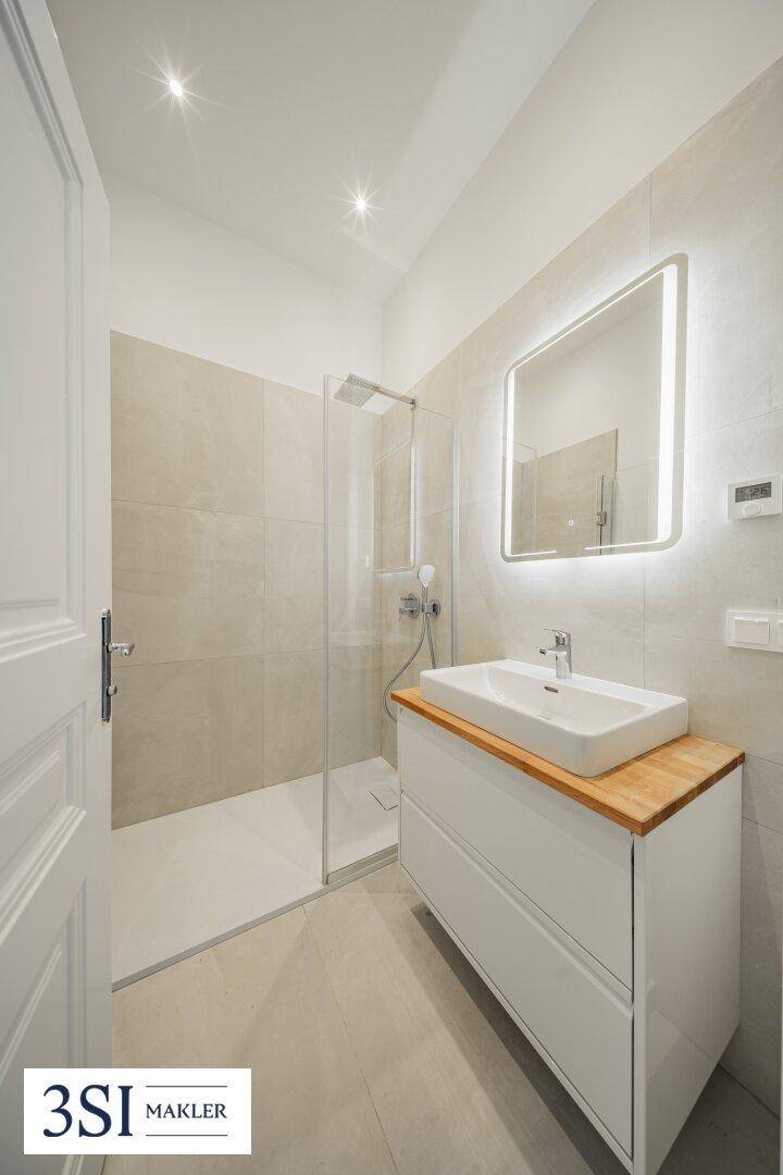 Modernes Badezimmer mit ebenerdiger Dusche, stilvollem Waschtisch und beleuchtetem Spiegel.