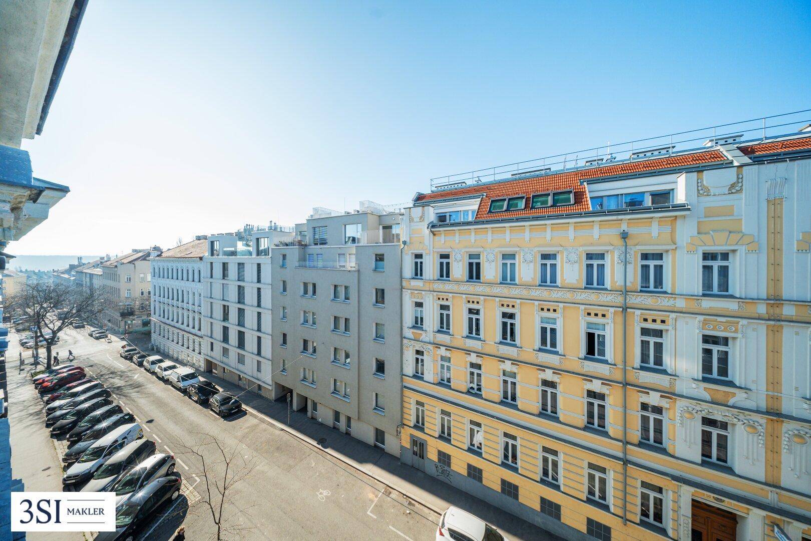 Weitblick über eine belebte Stadtstraße mit historischen und modernen Gebäuden unter blauem Himmel.
