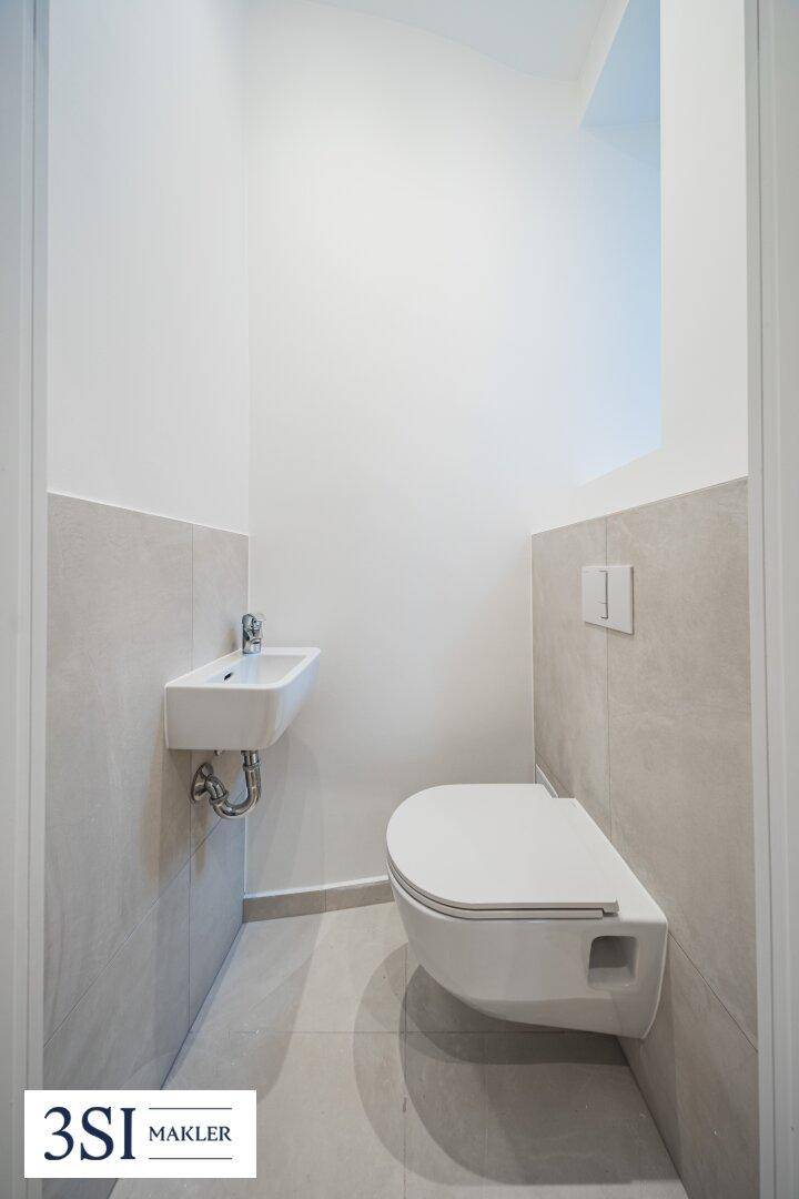 Kompaktes Gäste-WC mit wandhängender Toilette und kleinem Handwaschbecken in modernem Design.