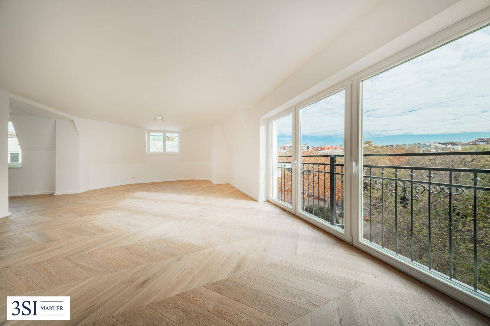 Heller Raum mit Fischgrätparkett, großen Fenstern und Zugang zu einem französischen Balkon mit Weitblick.