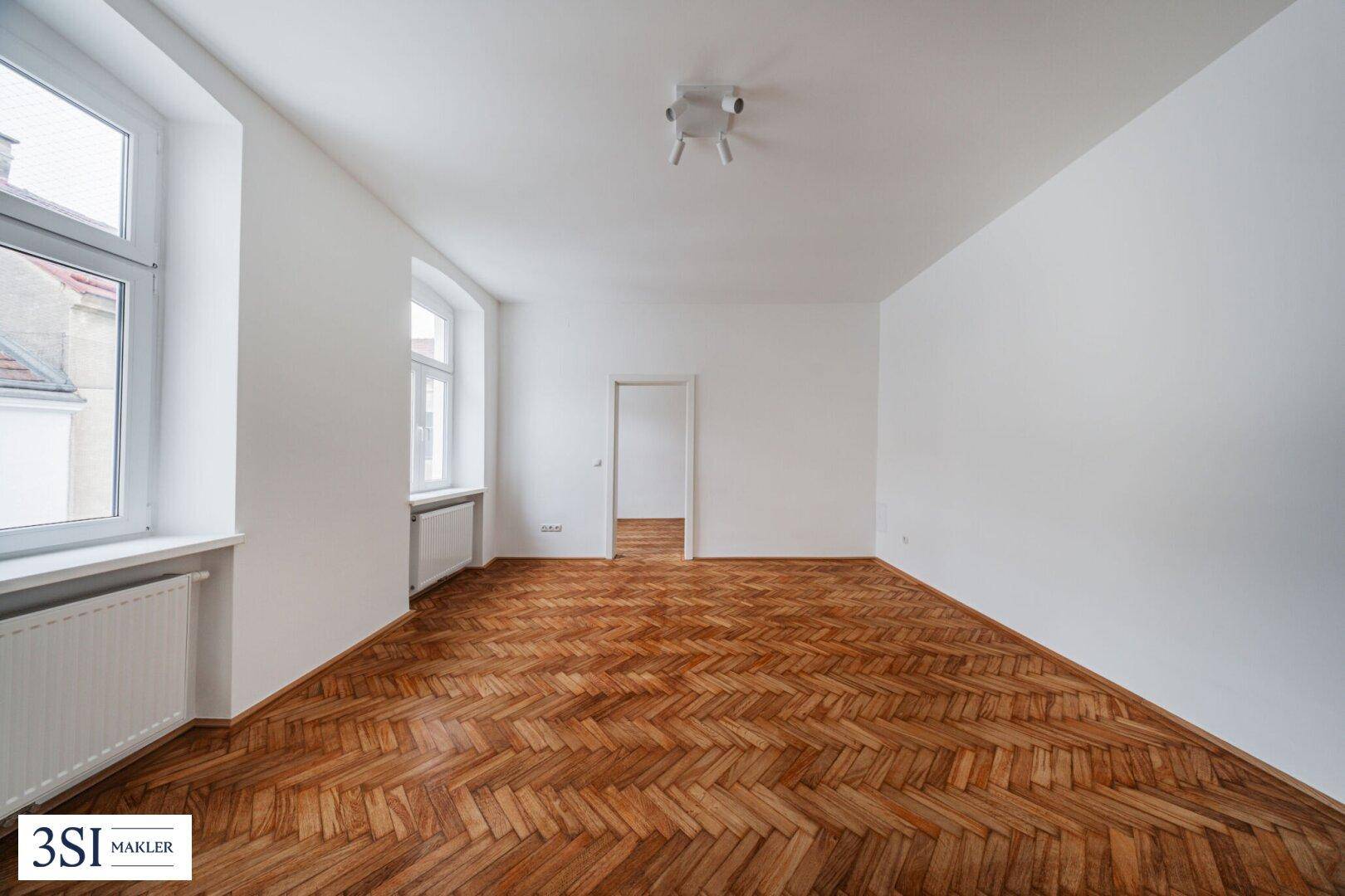 Geräumiges, helles Zimmer mit klassischem Fischgrätparkett und großen Fenstern.