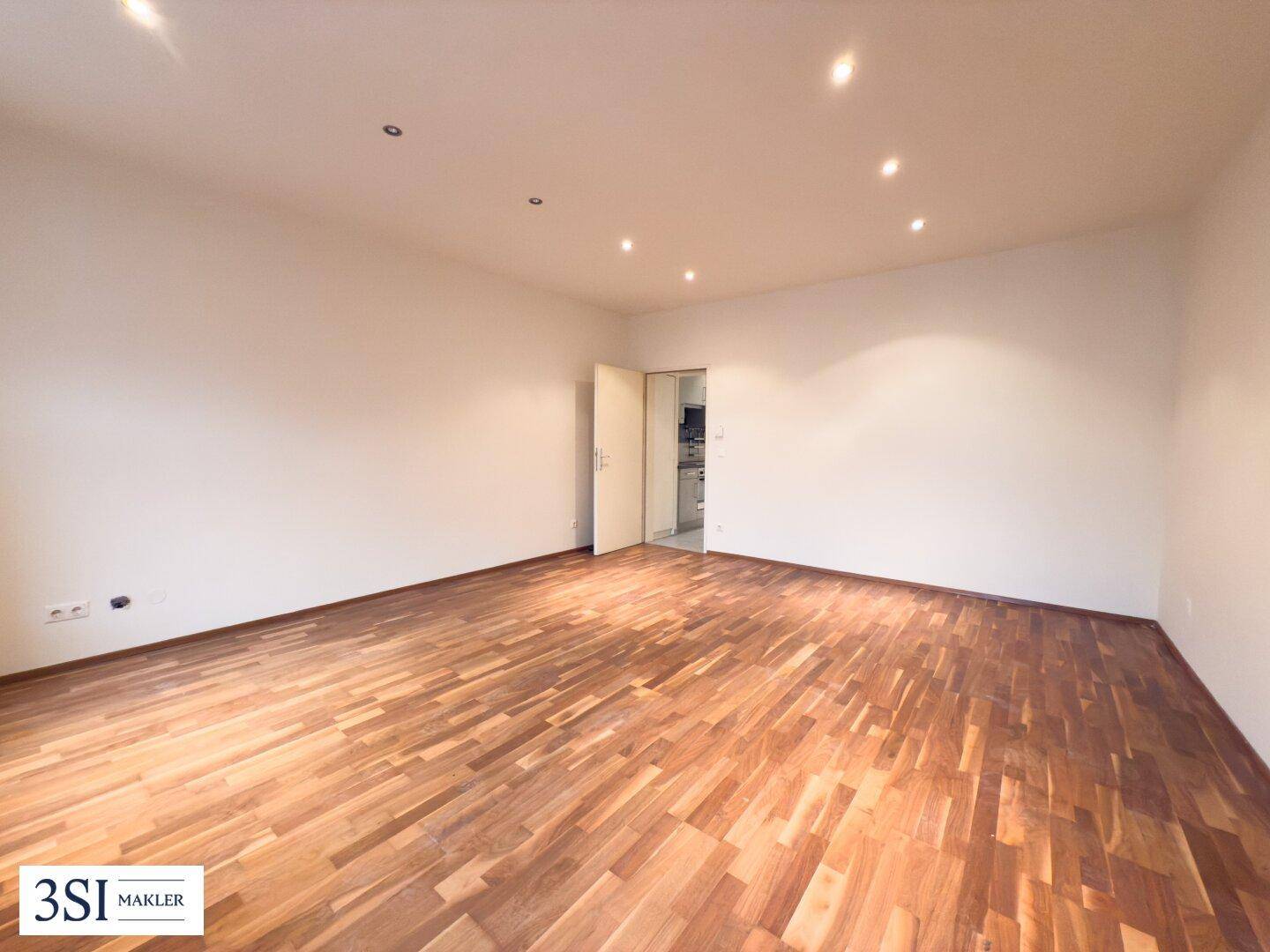 Geräumiges Wohnzimmer mit hellem Parkettboden und integrierten Deckenstrahlern, bereit zur individuellen Gestaltung.