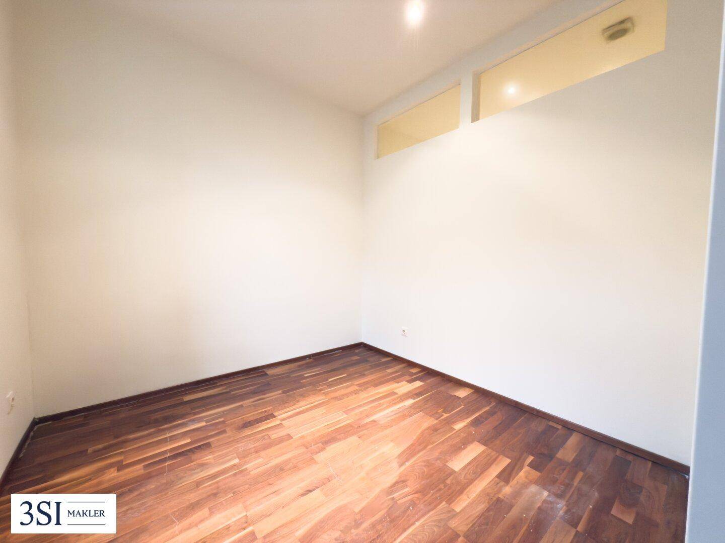 Leeres Zimmer mit Holzboden und indirekter Beleuchtung durch Oberlichter, ideal für Schlaf- oder Arbeitsbereich.