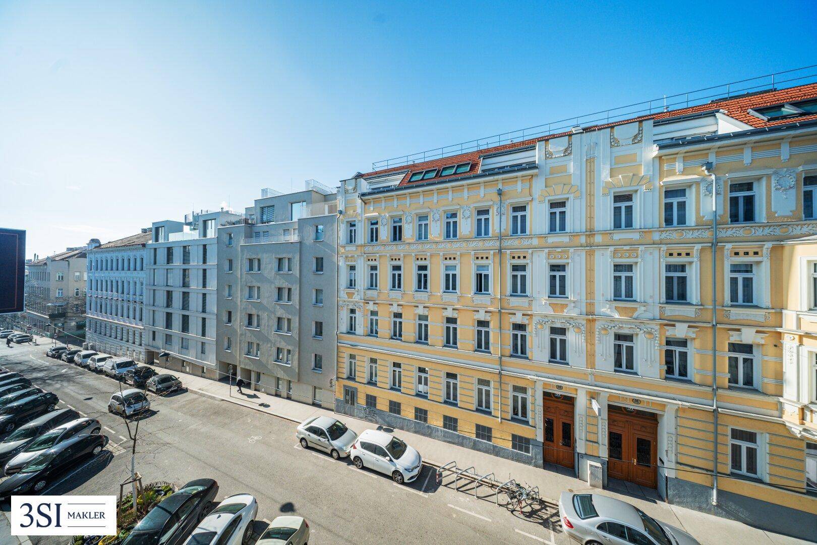 Ansicht der Wohngebäude entlang der Straße mit parkenden Autos und klarem Himmel.