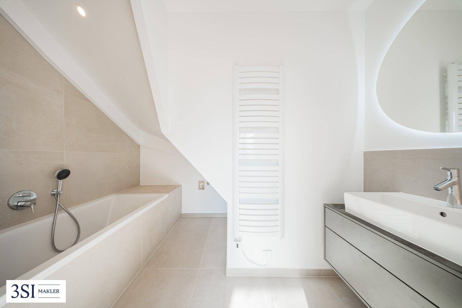 Helles Badezimmer mit Badewanne, Einzelwaschbecken und beheiztem Handtuchhalter unter der Dachschräge.