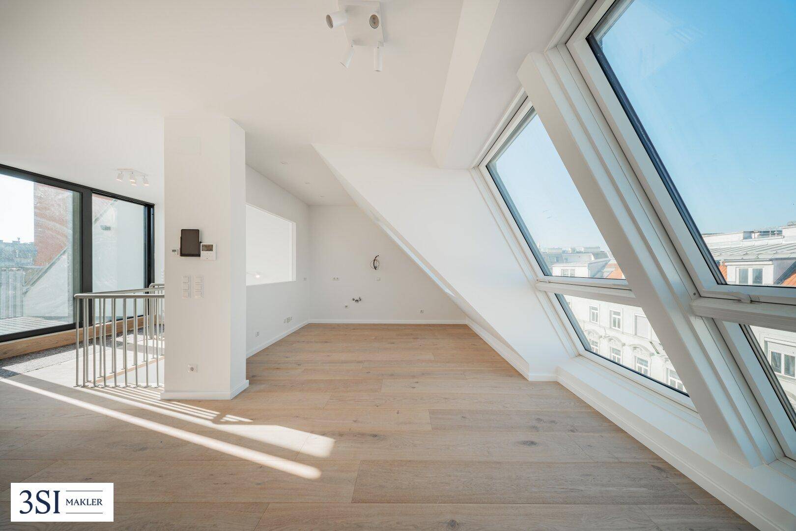 Lichtdurchfluteter Wohnbereich im Dachgeschoss mit Holzboden, großen Fenstern und Zugang zu einem Balkon.