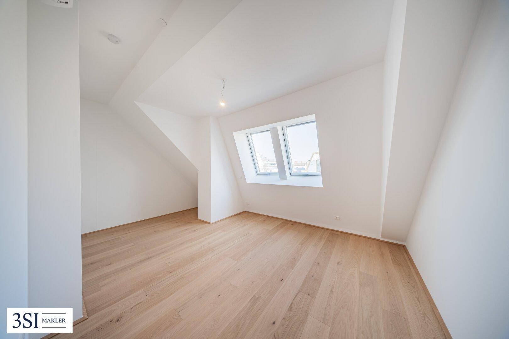 Ruhiges Dachgeschosszimmer mit Holzboden und einem großen Dachfenster.