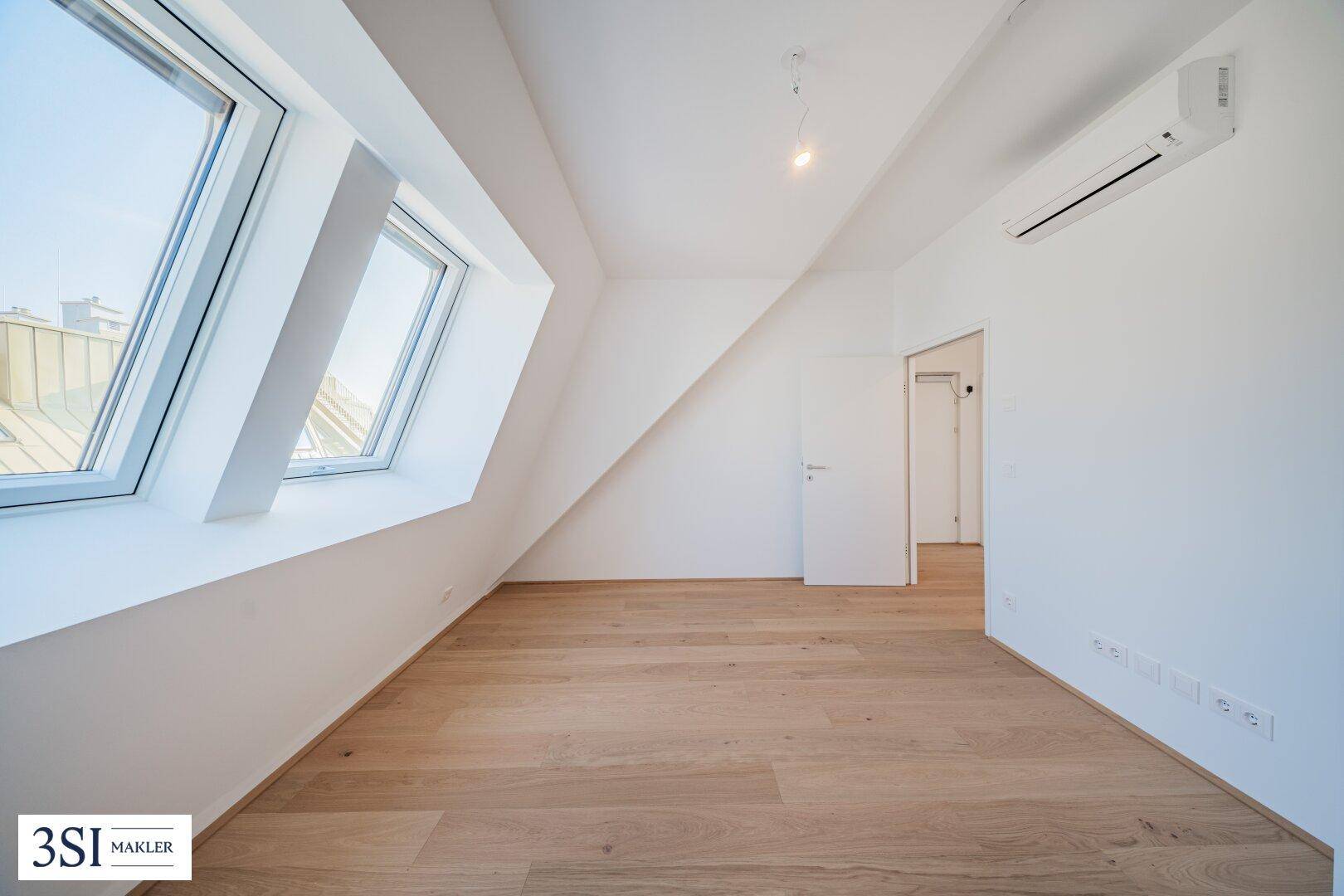 Helles Zimmer im Dachgeschoss mit Holzboden, Dachfenstern und Klimaanlage.